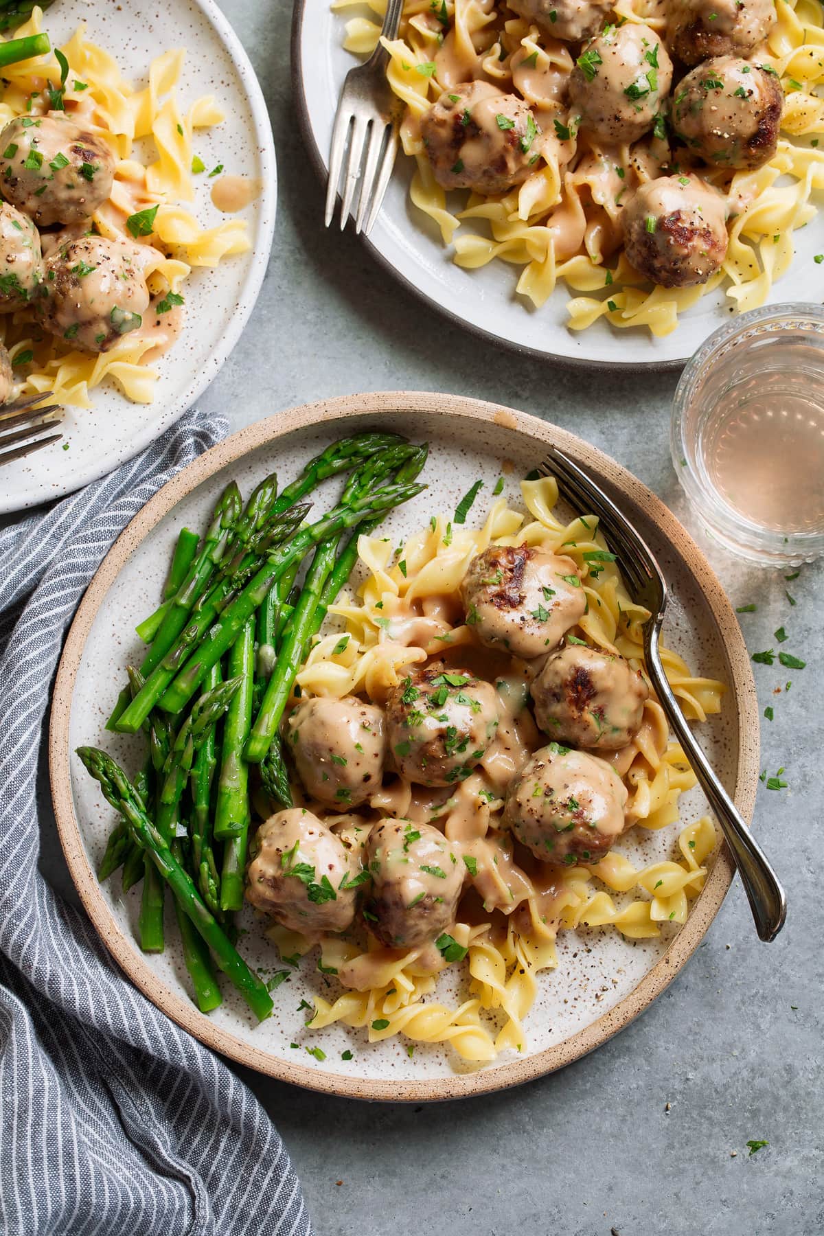 Swedish Meatballs Three servings of Swedish meatballs on plates. Meatballs are laying over egg noodles and served with a side of steamed asparagus.