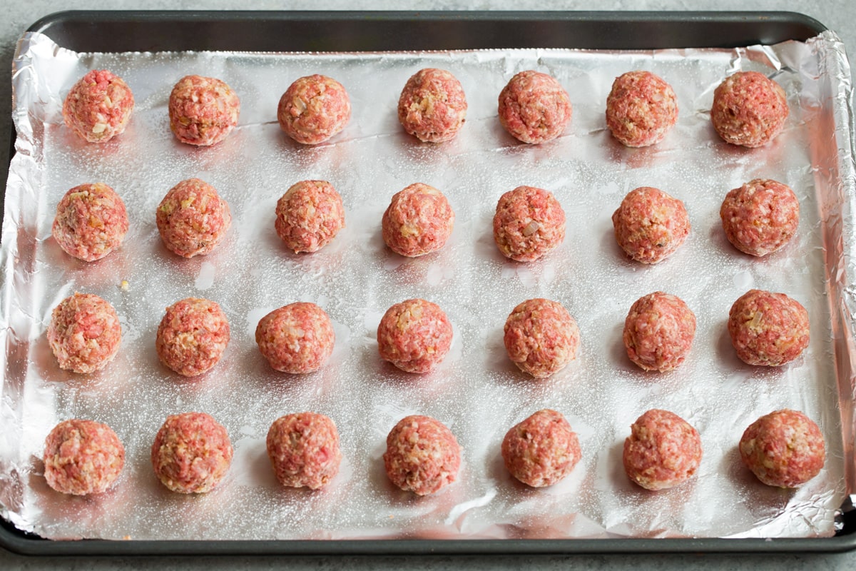 BEST Swedish Meatballs Recipe (Oven Baked)! 28 shaped Swedish meatballs on foil lined baking sheet, shown before baking.
