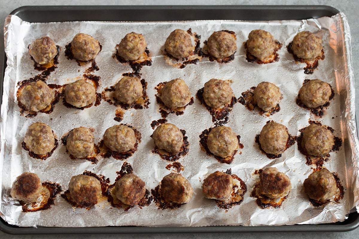 BEST Swedish Meatballs Recipe (Oven Baked)! 28 shaped Swedish meatballs on foil lined baking sheet, shown after baking.