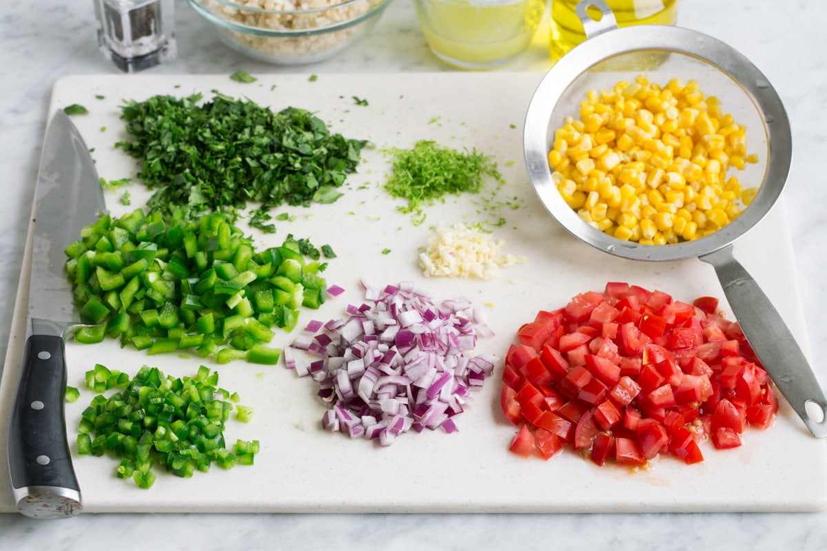 Fiesta Rice - healthy, easy and so flavorful! Perfect side to seafood, chicken and Mexican dishes. Or just eat it on it's own, it's so filling! #rice #ricerecipe #mexican #blackbeans Chopped vegetables on a cutting board with corn in a colander to drain and rice in the background in a bowl.