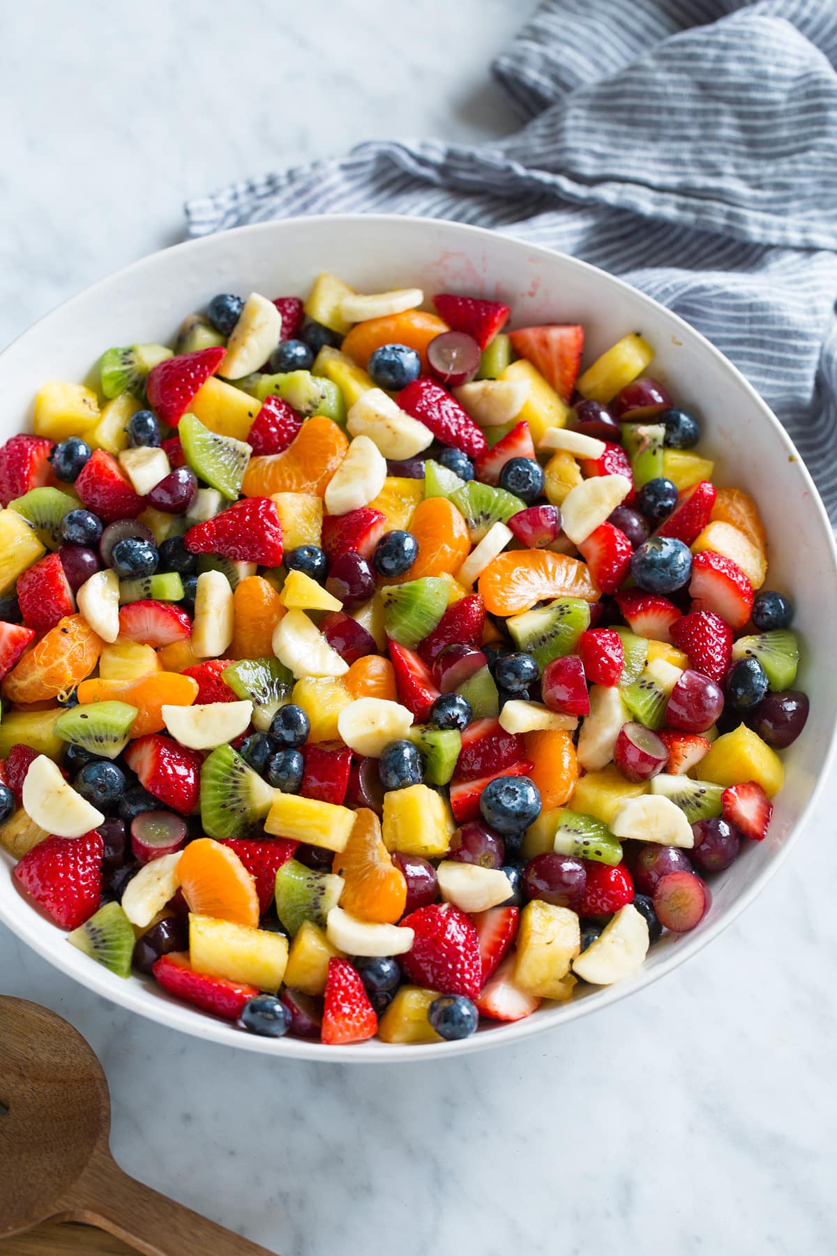 Honey Lime Rainbow Fruit Salad Fruit Salad with chopped fresh fruit in a large salad bowl set over a marble surface.