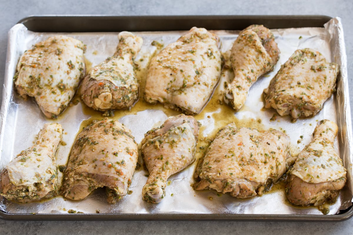 Jerk Chicken Baked or Grilled Raw marinated chicken pieces on a foil lined baking sheet.