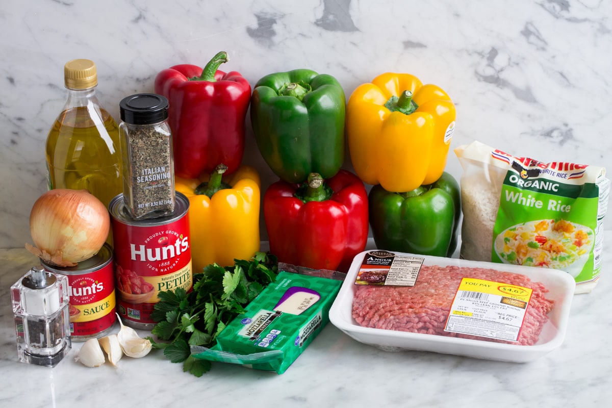Stuffed Peppers Ingredients to make stuffed peppers show here including bell peppers, ground beef, tomato sauce, diced tomatoes, garlic, onion, italian seasoning, mozzarella, white rice, olive oil, parsley.