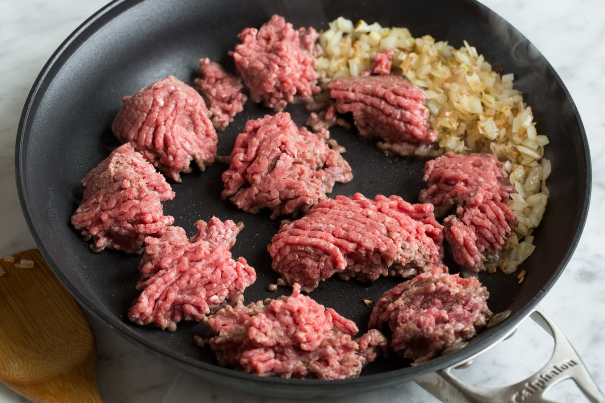 Stuffed Peppers Showing how to make stuffed peppers, browning ground beef in a skillet along with yellow onions.