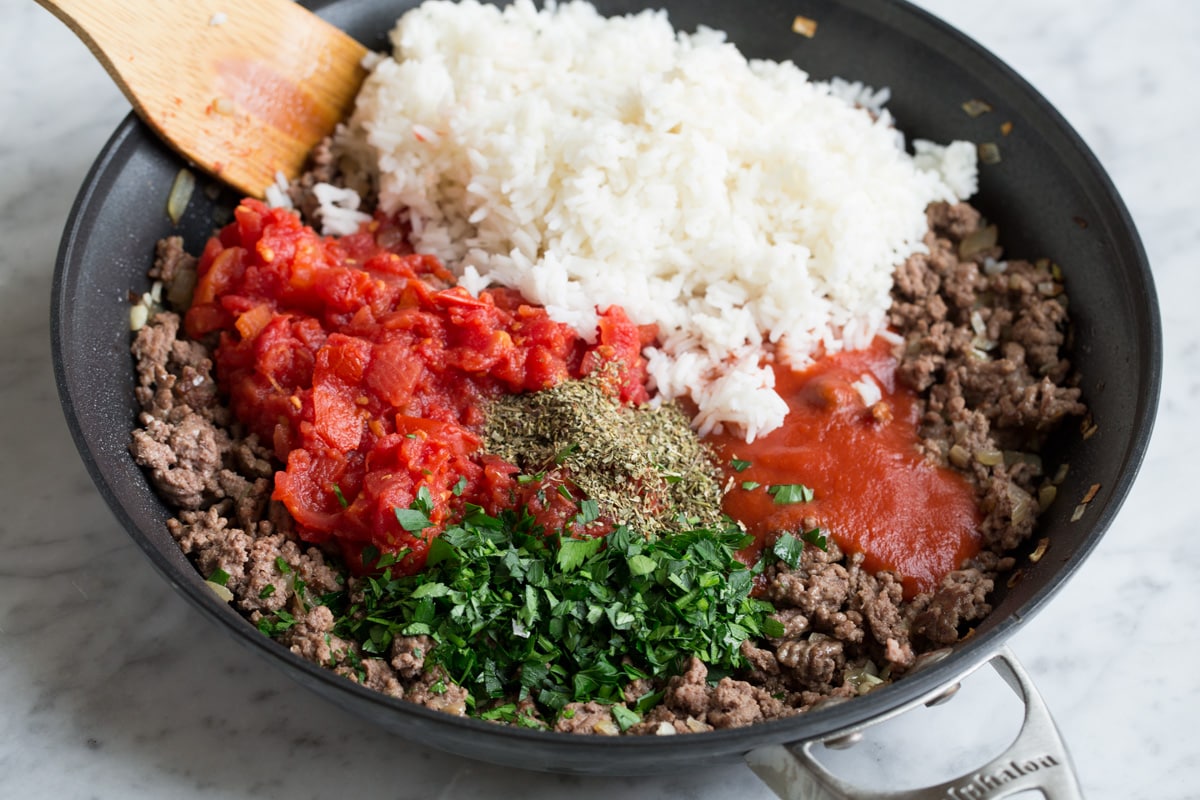 Stuffed Peppers Adding cooked rice, tomatoes, tomato sauce, and herbs to ground beef mixture in skillet.