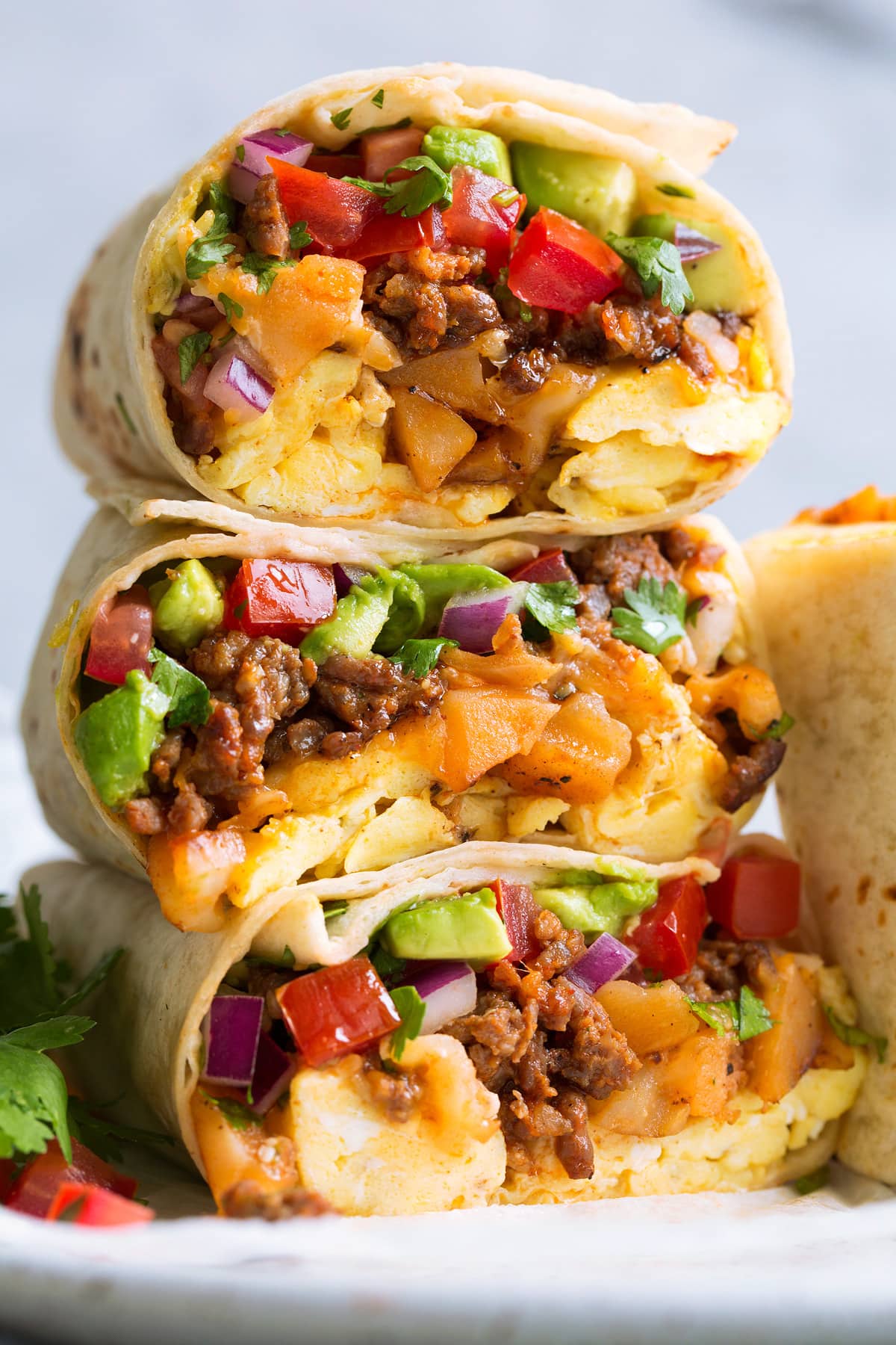 Breakfast Burritos Stack of breakfast burritos with eggs, chorizo sausage, potatoes, cheese, pico de gallo and avocado.