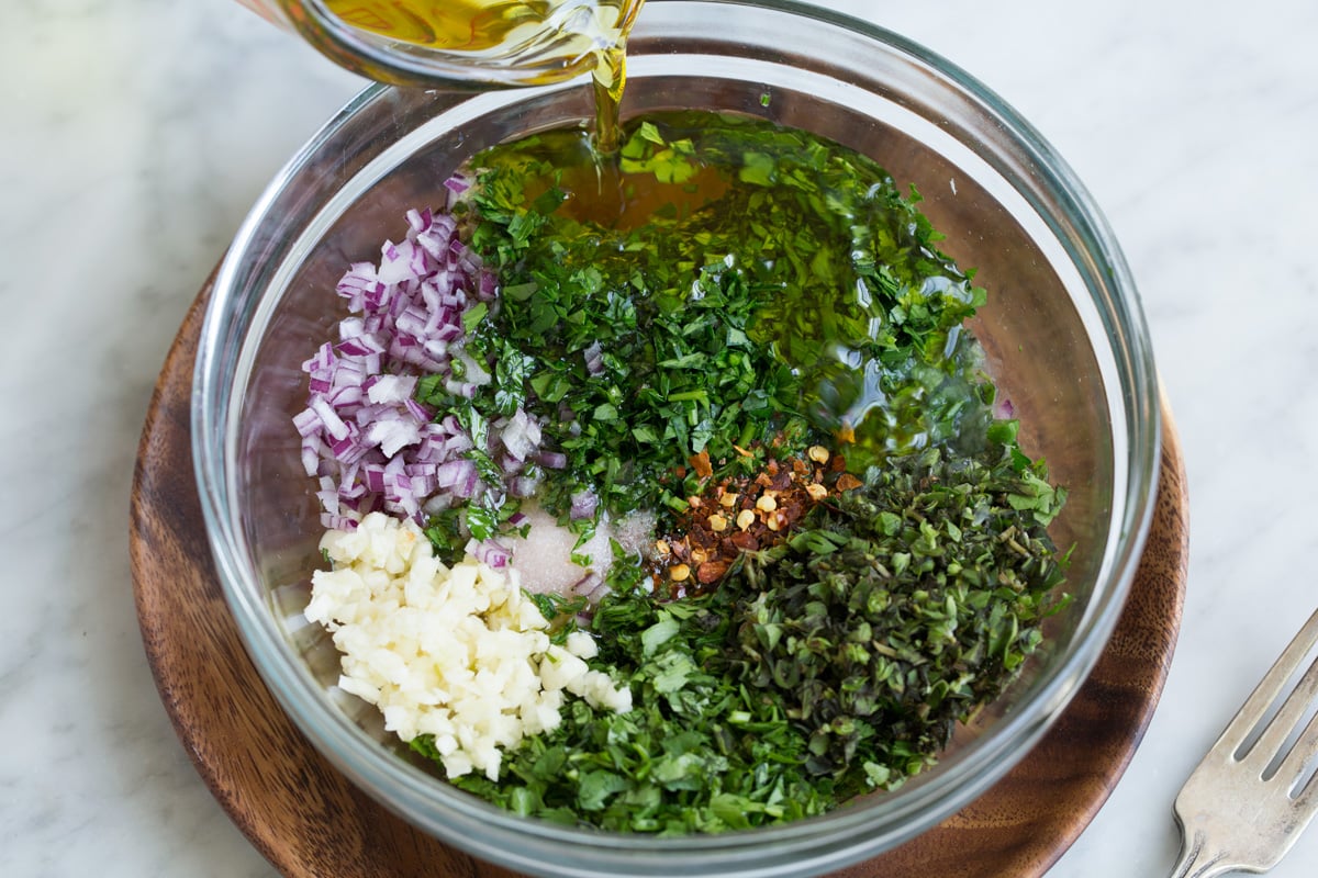 Best Chimichurri Sauce Showing how to make chimichurri. Mixing parsley, cilantro, oregano, onion, garlic, red pepper flakes, olive oil, lemon and red wine vinegar in a glass mixing bowl.