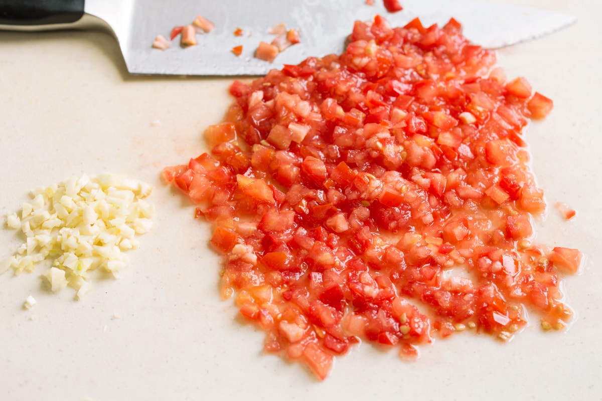 Mexican Rice Finely chopped tomatoes and garlic on a cutting board with a knife on the side.