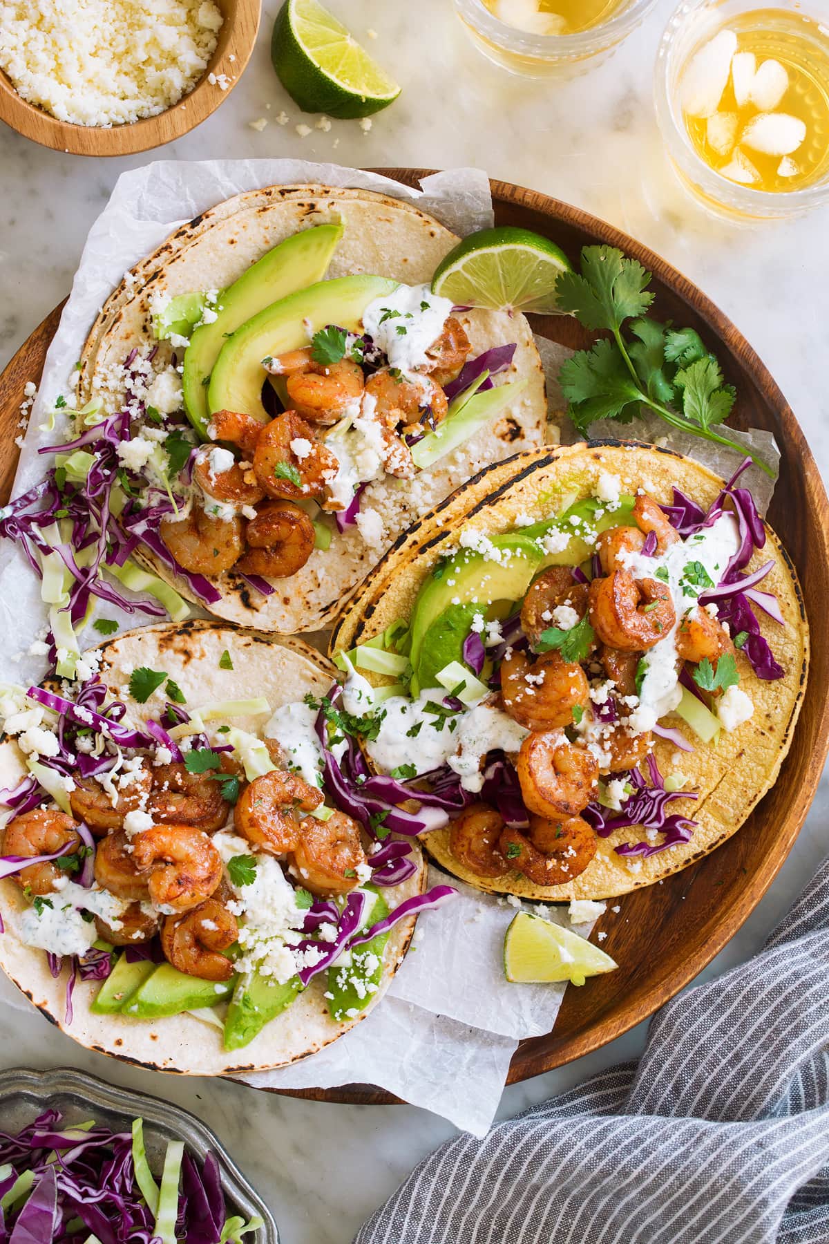 Shrimp Tacos with Cilantro Lime Crema Shrimp Tacos on a wooden serving plate on parchment. Tacos are topped with cabbage, avocado, and cilantro lime crema.