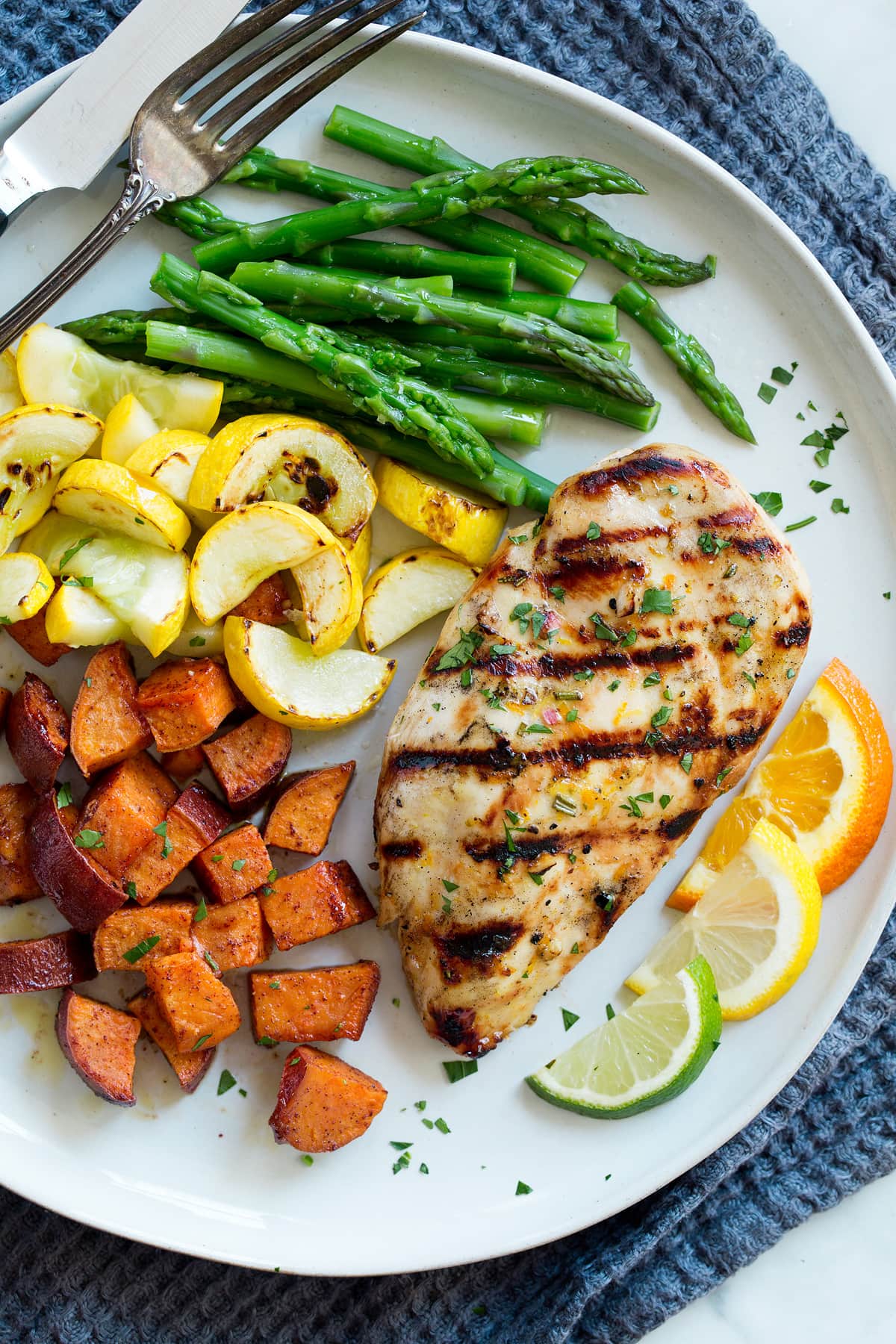 Triple Citrus Chicken Marinade - perfectly bright and refreshing! Total upgrade to plan chicken breasts or thighs. Such a delicious summer recipe! #chicken #marinade #recipe #dinner #grilled Marinated chicken on a serving plate with a side of asparagus, yellow squash, sweet potatoes and citrus slices.