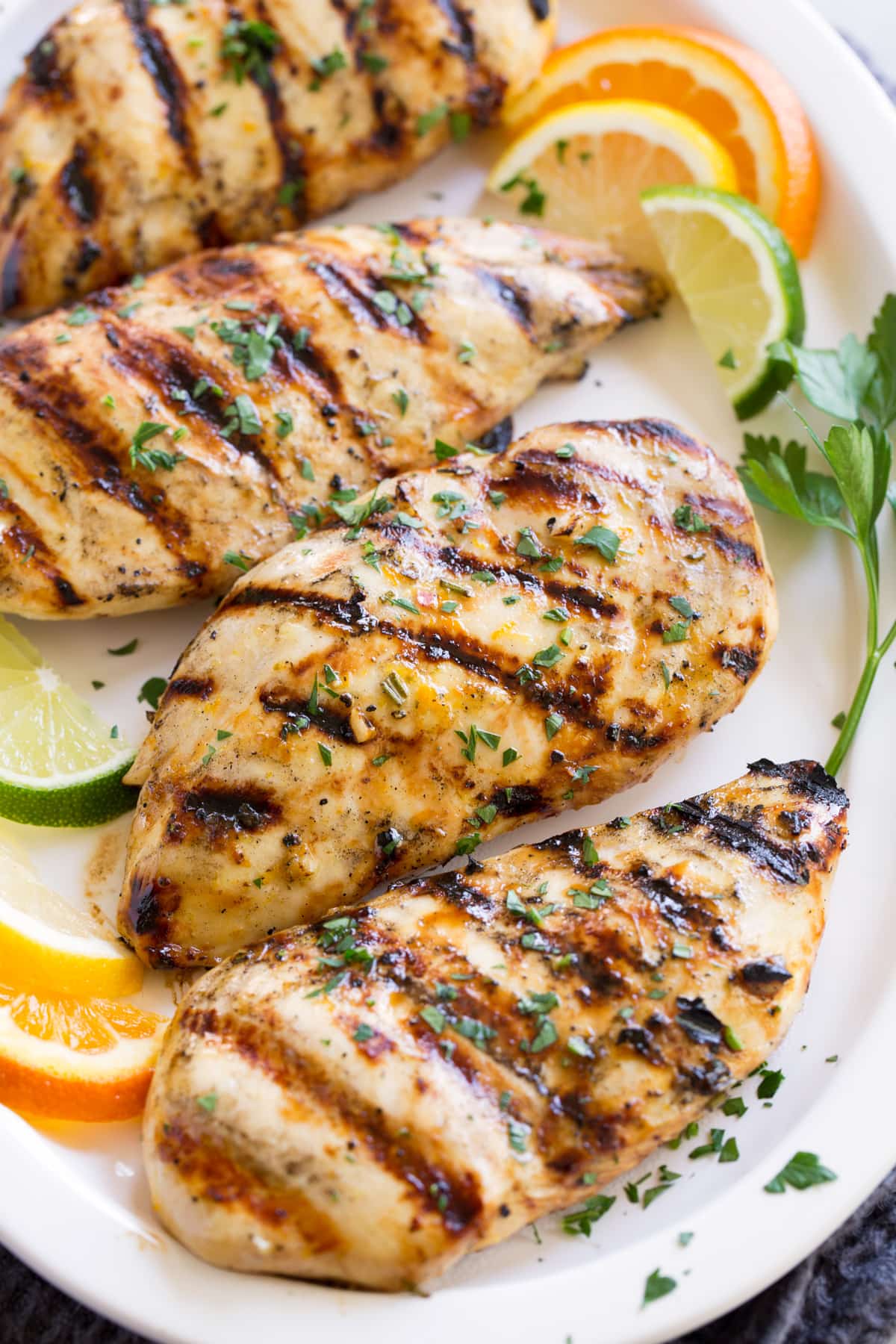 Triple Citrus Chicken Marinade - perfectly bright and refreshing! Total upgrade to plan chicken breasts or thighs. Such a delicious summer recipe! #chicken #marinade #recipe #dinner #grilled Row of marinated grilled chicken on a white serving plate.
