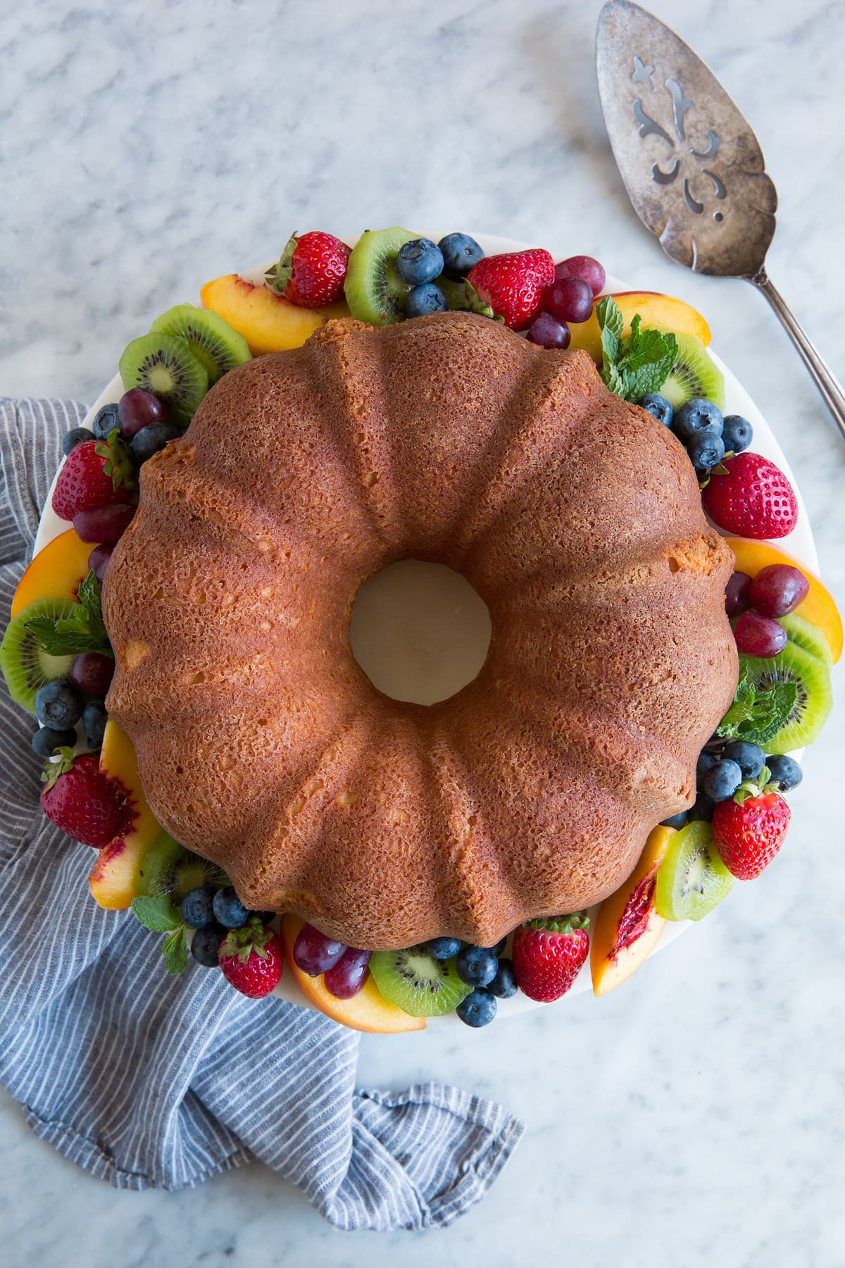 Pound Cake Overhead image of whole pound cake on a cake stand with colorful fresh fruit around edges.