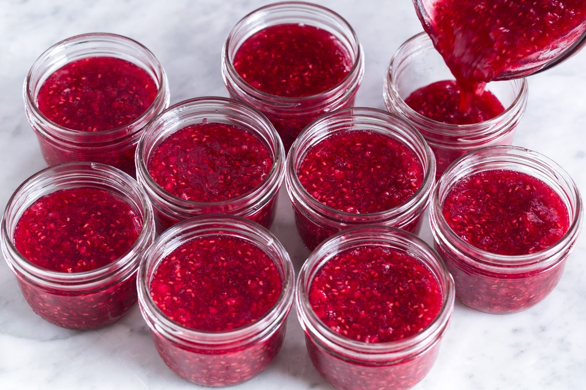 Easy Homemade Raspberry Freezer Jam - no canning skills or equipment required! This is my all time favorite jam! I've been making it for 10+years, it's the only jam I make now. Everyone always loves it and it freezes for up to 1 year! #jam #freezerjam #homeamdejam #easyrecipe Pouring jam into glass jars.