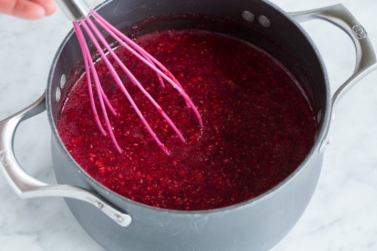 Easy Homemade Raspberry Freezer Jam - no canning skills or equipment required! This is my all time favorite jam! I've been making it for 10+years, it's the only jam I make now. Everyone always loves it and it freezes for up to 1 year! #jam #freezerjam #homeamdejam #easyrecipe Whisking raspberries into sugar mixture in saucepan,