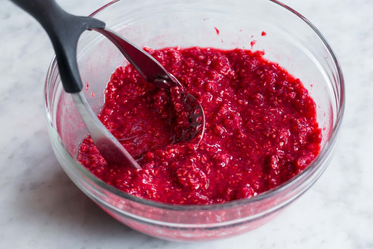 Easy Homemade Raspberry Freezer Jam - no canning skills or equipment required! This is my all time favorite jam! I've been making it for 10+years, it's the only jam I make now. Everyone always loves it and it freezes for up to 1 year! #jam #freezerjam #homeamdejam #easyrecipe Showing how to make raspberry jam. Staring here by crushing raspberries in a glass mixing bowl with a potato masher.