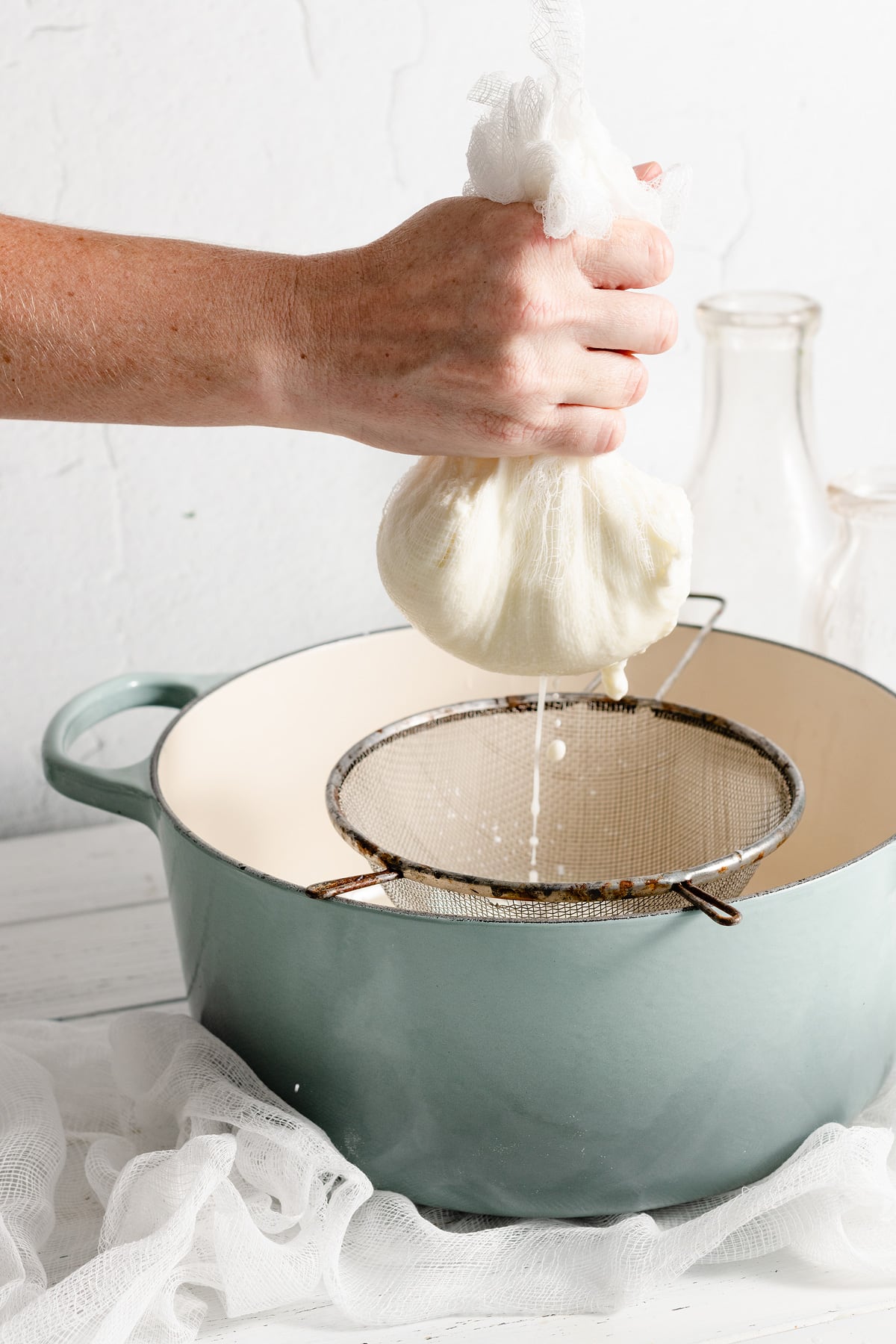 Homemade Ricotta Cheese - the BEST ricotta you'll try! It's so much better than store bought and incredibly easy to make! It's delicious in savory and sweet dishes and you can use the leftovers for toast. #ricotta #cheese #recipe #homemade #italianrecipes Hand holding cheesecloth full of ricotta cheese that is draining of liquid into a pot.