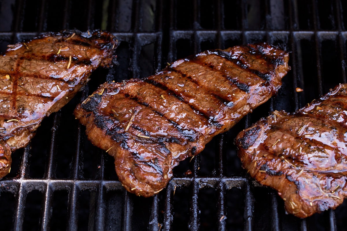 The BEST Steak Marinade! Made with balsamic vinegar and a handful of other pantry staples. A summer must have recipe! #steak #marinade Three steaks on the grill.
