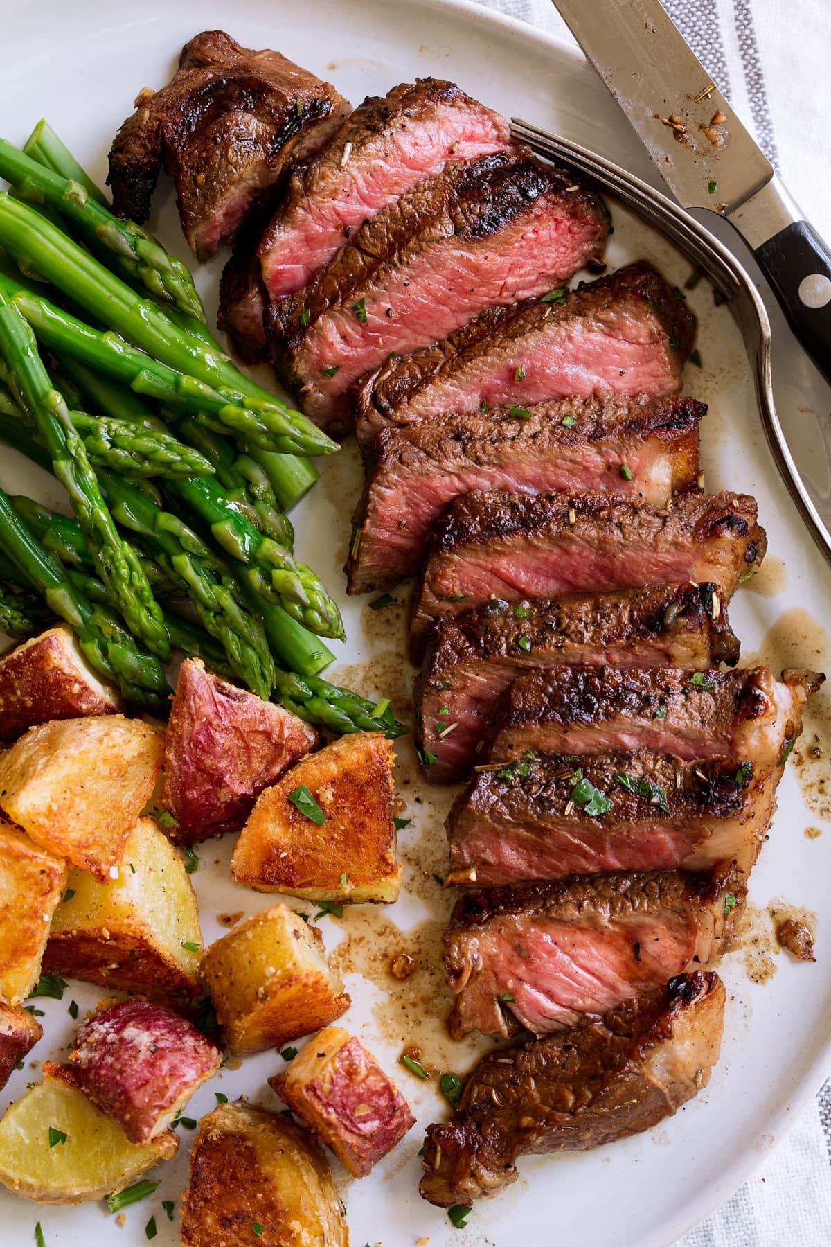 The BEST Steak Marinade! Made with balsamic vinegar and a handful of other pantry staples. A summer must have recipe! #steak #marinade Marinated grilled steak on a serving plate with a side of asparagus and potatoes.