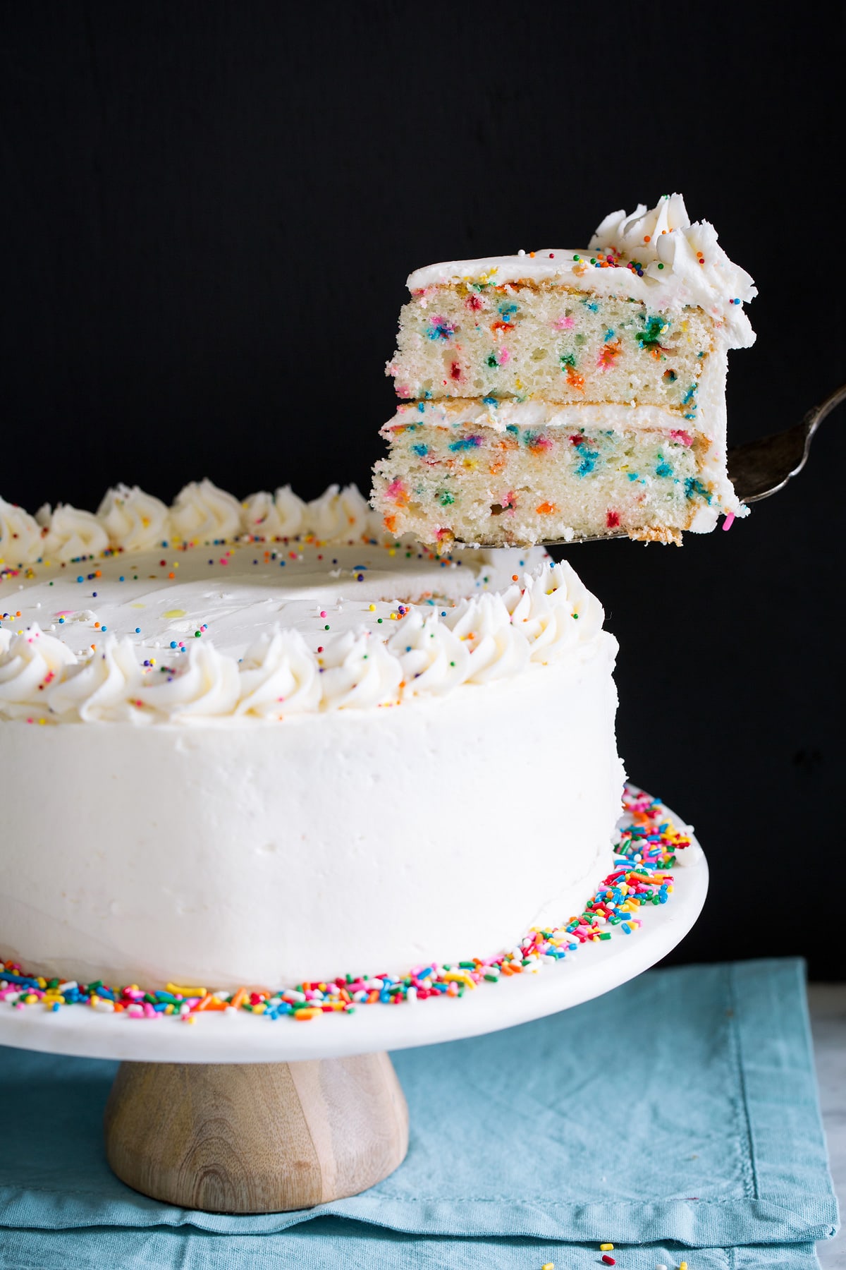 Birthday Cake - the perfect funfetti sprinkled cake! It's perfectly soft and fluffy and amazingly delicious! My kids absolute favorite cake! #cake #birthdaycake #dessert #birthday Lifting a single slice with a serving spatula from a whole cake.