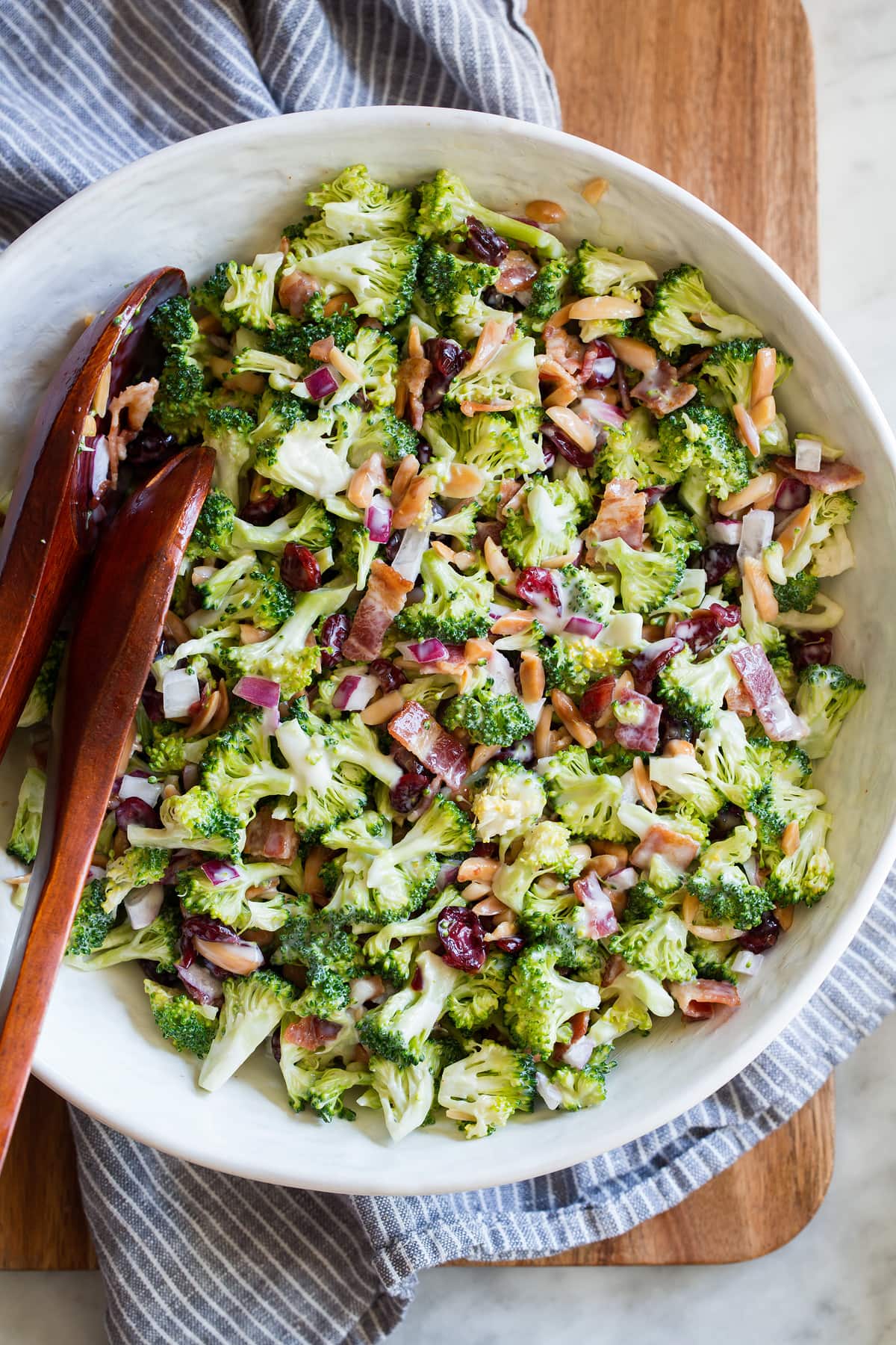 Perfect Broccoli Salad! A classic must have recipe! Made with crisp pieces of tiny broccoli florets, salty bacon, sweet dried cranberries, bright red onion, nutty toasted almonds and a creamy rich dressing. #broccoli #salad #summer #sidedish #recipe Broccoli salad in a serving bowl with serving spoons.