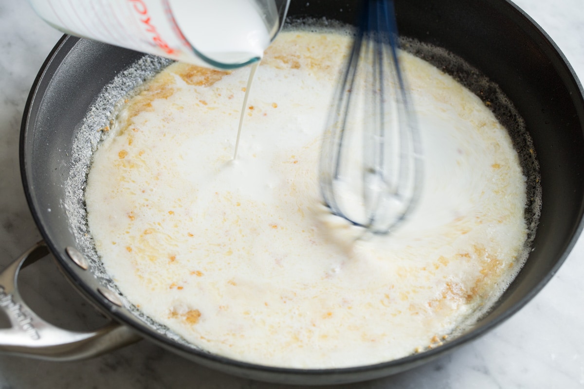 Best Alfredo Sauce - made with half milk and half cream so it's not too heavy, and includes plenty of parmesan for incredible flavor! So easy and seriously delicious! #alfredosauce #alfredo #fettuccinealfredo #dinner #pasta Whisking cream into flour and butter mixture in skillet.