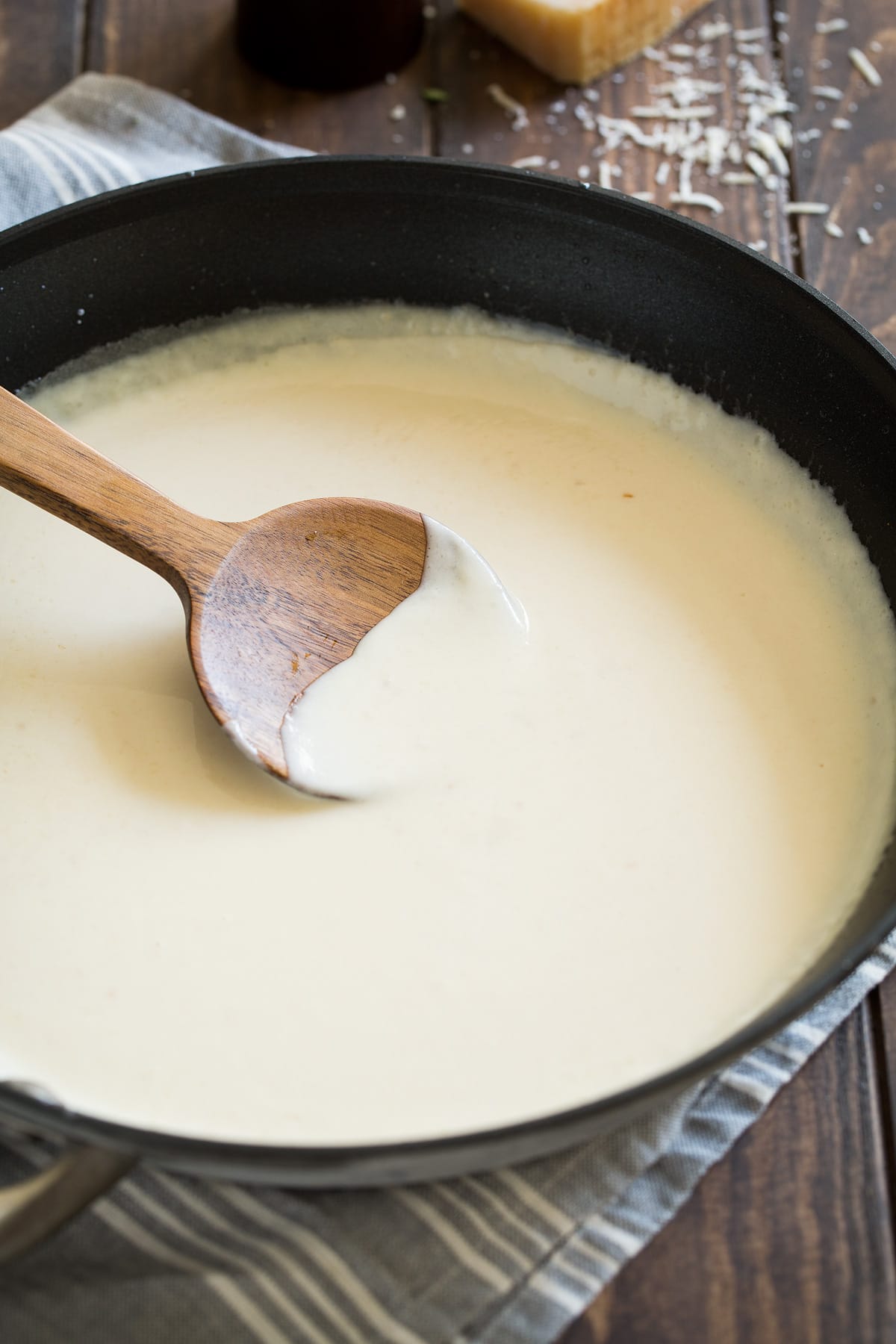 Best Alfredo Sauce - made with half milk and half cream so it's not too heavy, and includes plenty of parmesan for incredible flavor! So easy and seriously delicious! #alfredosauce #alfredo #fettuccinealfredo #dinner #pasta Alfredo sauce in a skillet with a wooden spoon.
