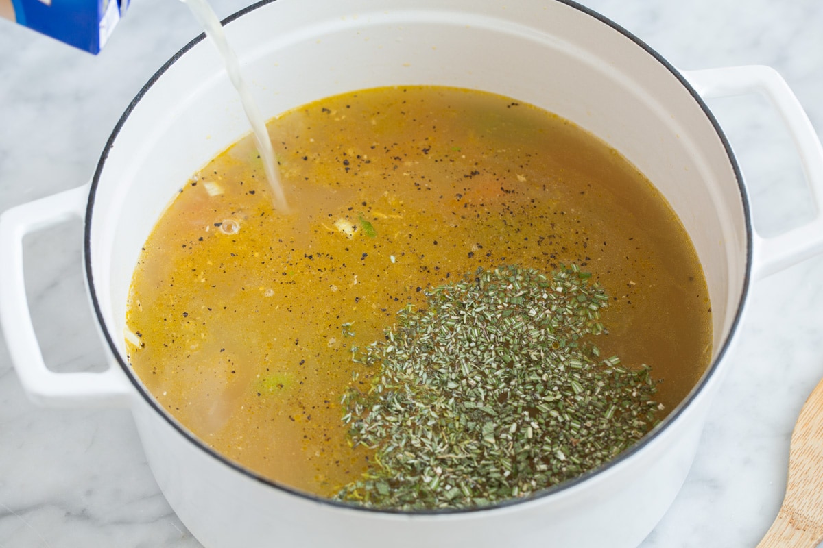 The BEST Quick and Easy Chicken Noodle Soup! This has been my go-to recipe for years. So easy and everyone always loves it! #chickennoodle #soup #dinner #chicken Pouring broth and herbs into pot.