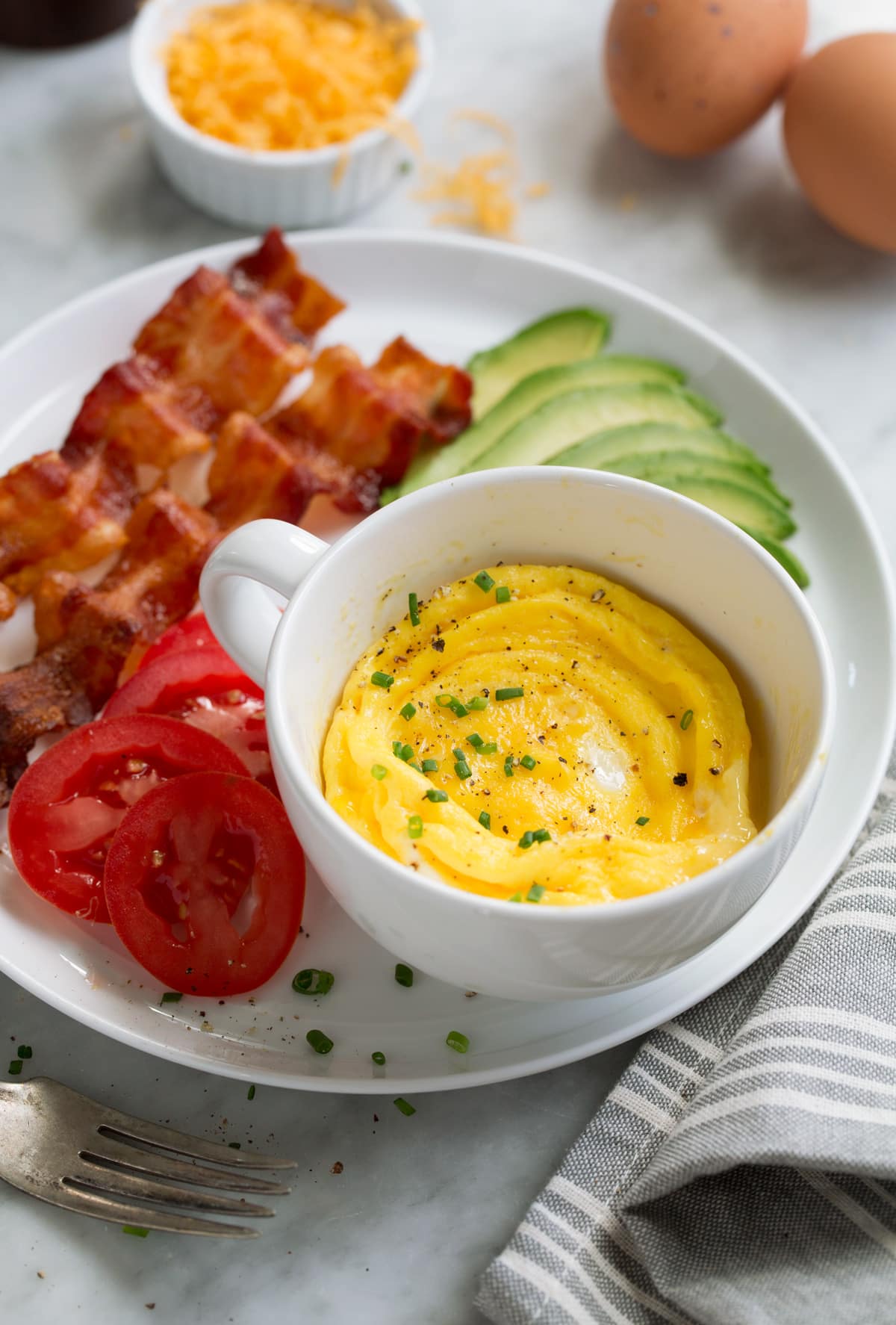 Microwave Scrambled Eggs in a Mug - super fast, super easy and always delicious! Perfect for breakfast sandwiches too! #eggs #breakfast #easybreakfast #quickbreakfast Microwave eggs with bacon, tomatoes and avocado to the side on a plate.