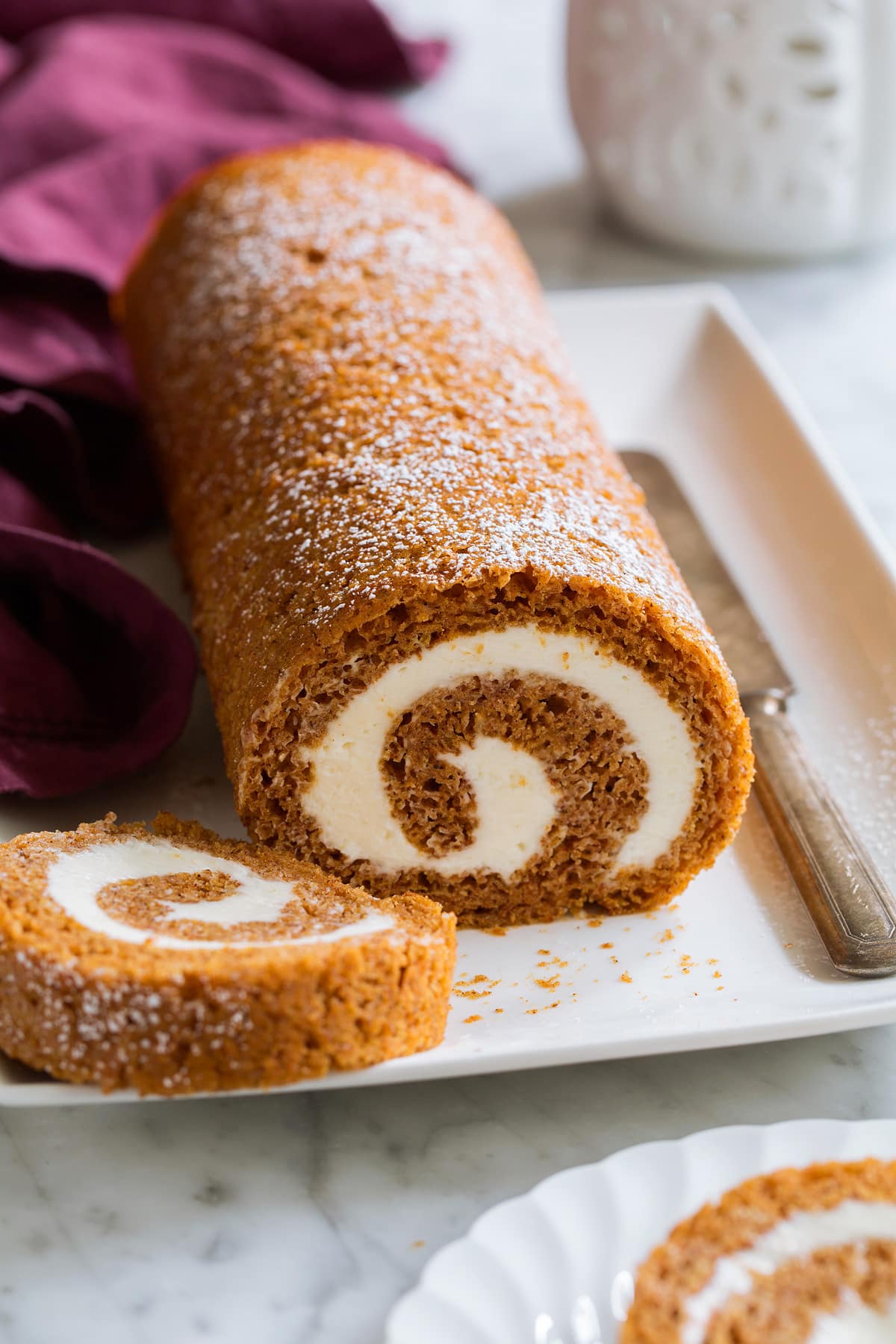 Pumpkin Roll Pumpkin Roll on a white platter with a slice cut to show swirled cream cheese filling.