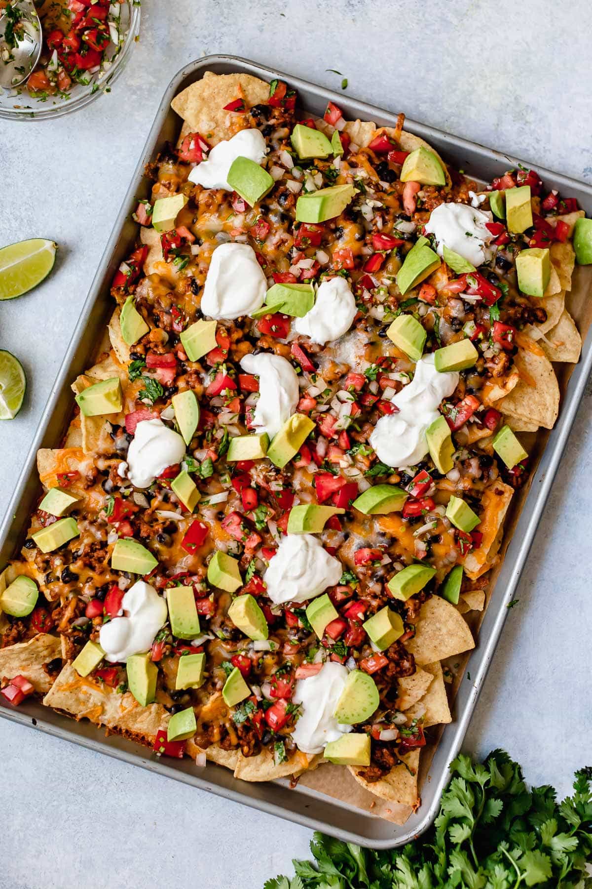 Easy Nachos - layered with seasoned beef and black beans, melty cheese, avocado and sour cream. SO GOOD! #nachos #sheetpan #beef #blackbeans #dinner #recipe Nachos on a sheet pan.