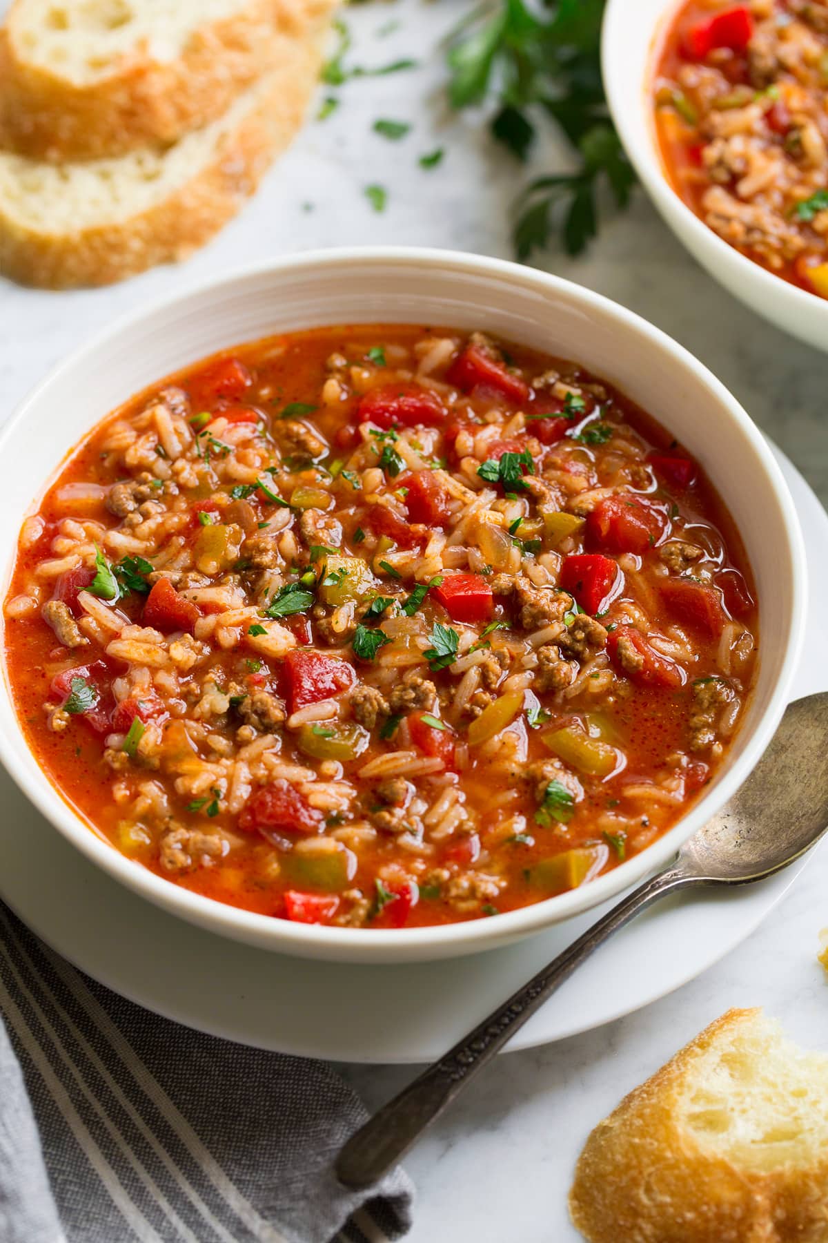 Stuffed Pepper Soup Single Serving of Stuffed Pepper Soup in a white serving bowl set over a white plate with a spoon and bread to the side.