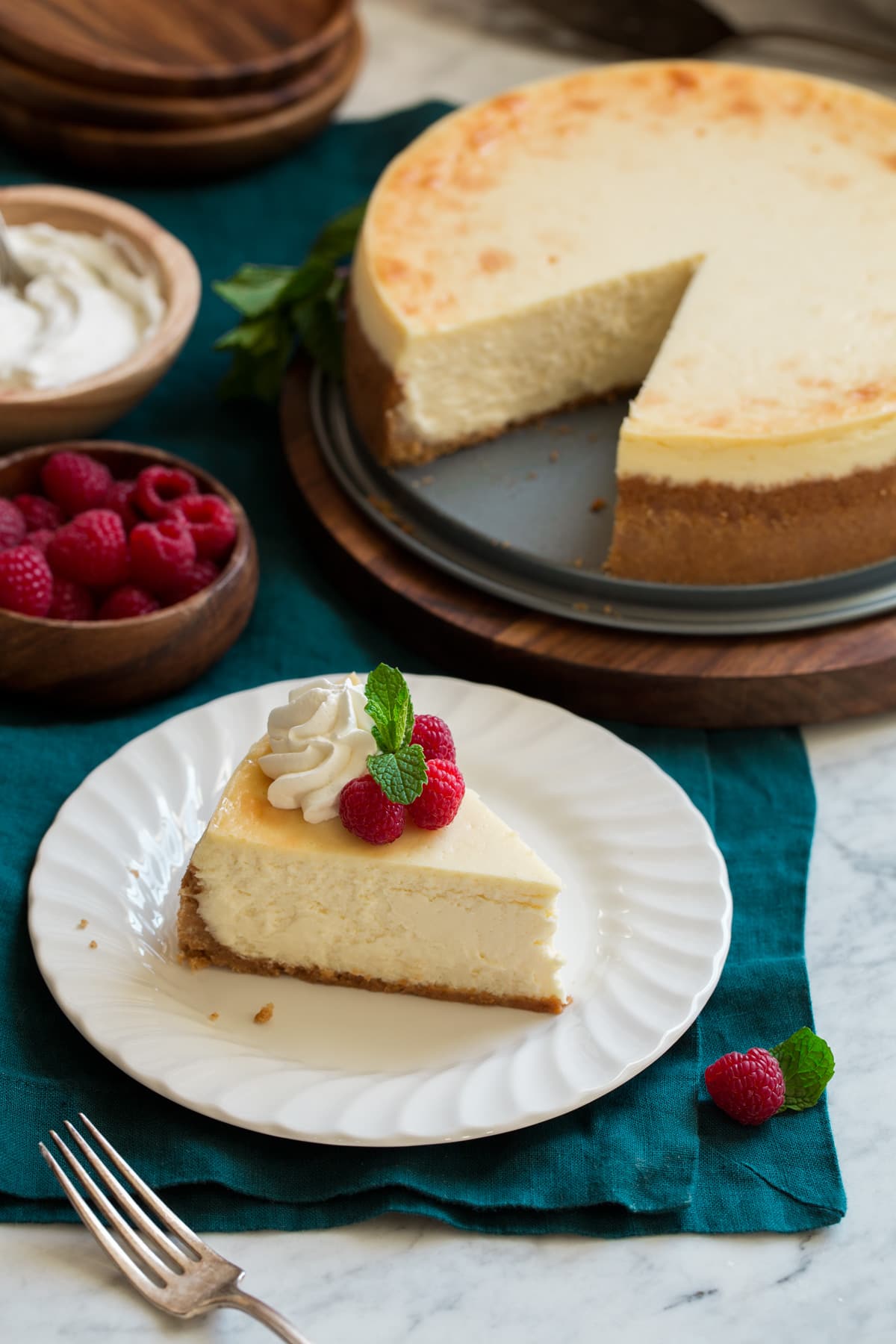 The BEST Cheesecake Recipe! One slice of cheesecake with whole cheesecake in background.