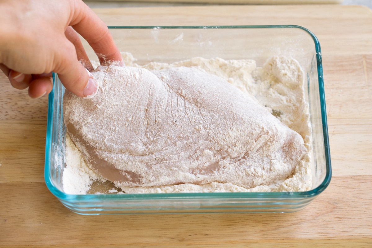 Creamy Lemon Romano Chicken Dredging pounded chicken breasts in flour in a shallow dish.