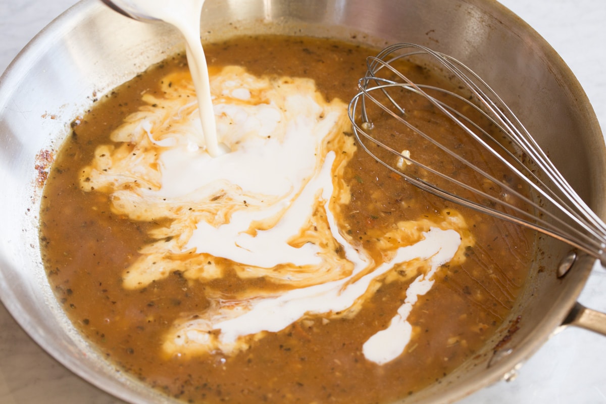 Creamy Lemon Romano Chicken Pouring cream into sauce mixture in skillet.