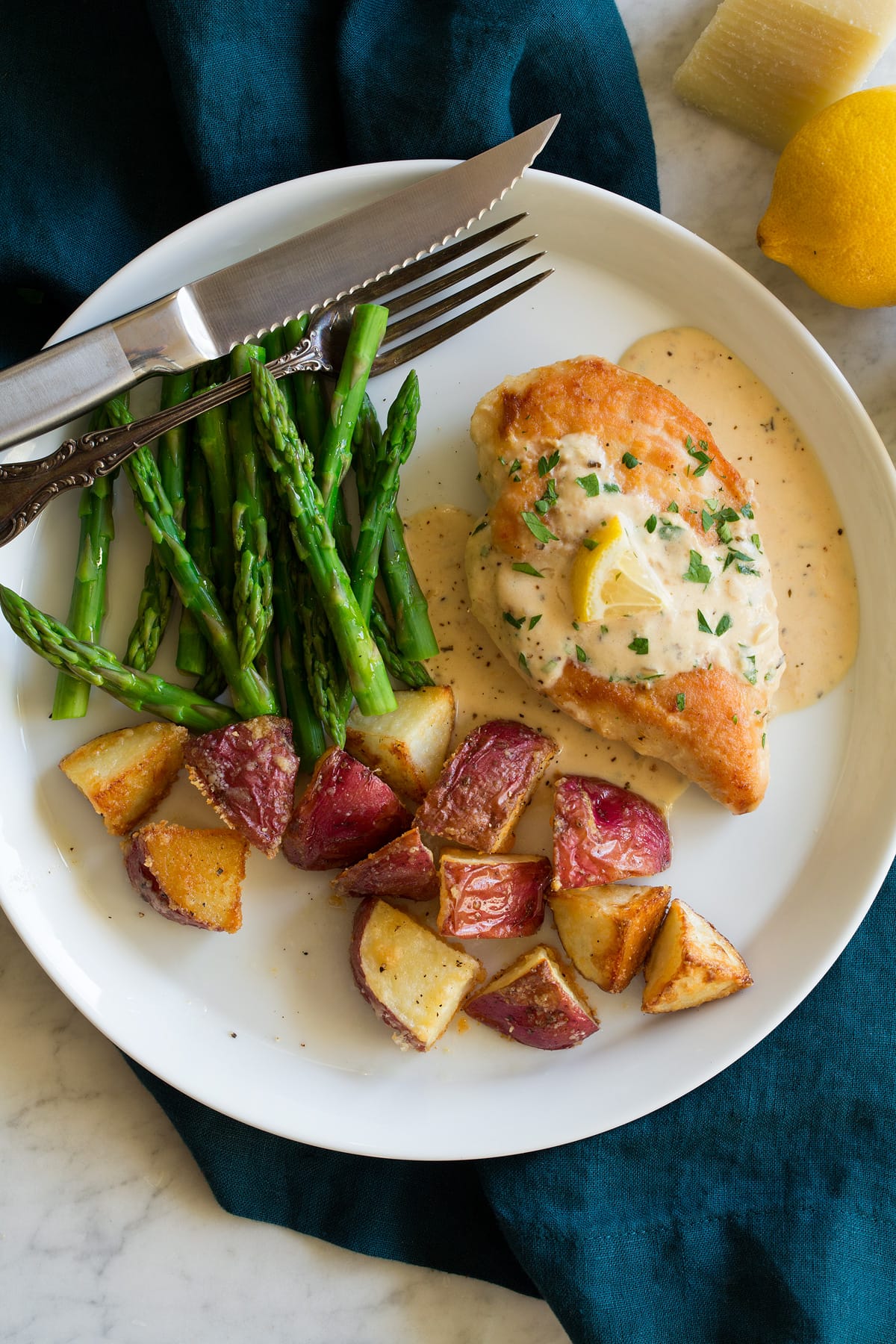Creamy Lemon Romano Chicken Plate with chicken breast topped with creamy lemon romano sauce and sides of potatoes and asparagus.