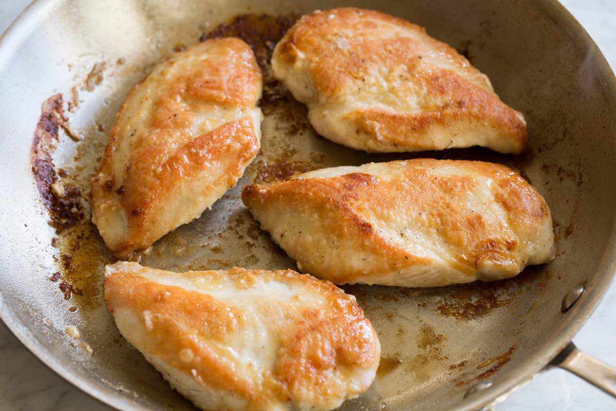 Creamy Lemon Romano Chicken Four golden brown seared chicken breasts in a large stainless steel skillet.