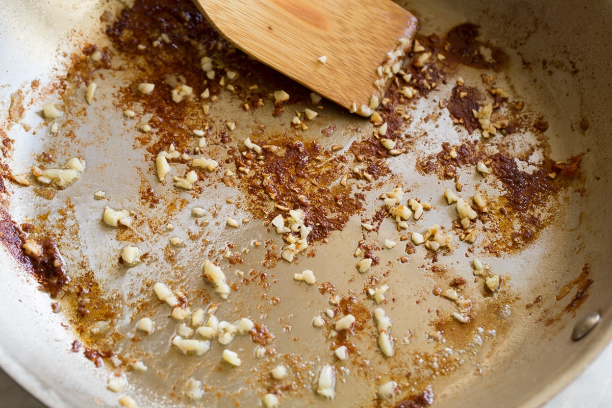 Creamy Lemon Romano Chicken Stainless steel skillet with sauteed garlic and browned bits on bottom.