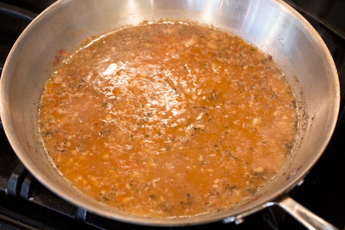 Creamy Lemon Romano Chicken Simmering and reducing sauce in the stove top in a large pan.