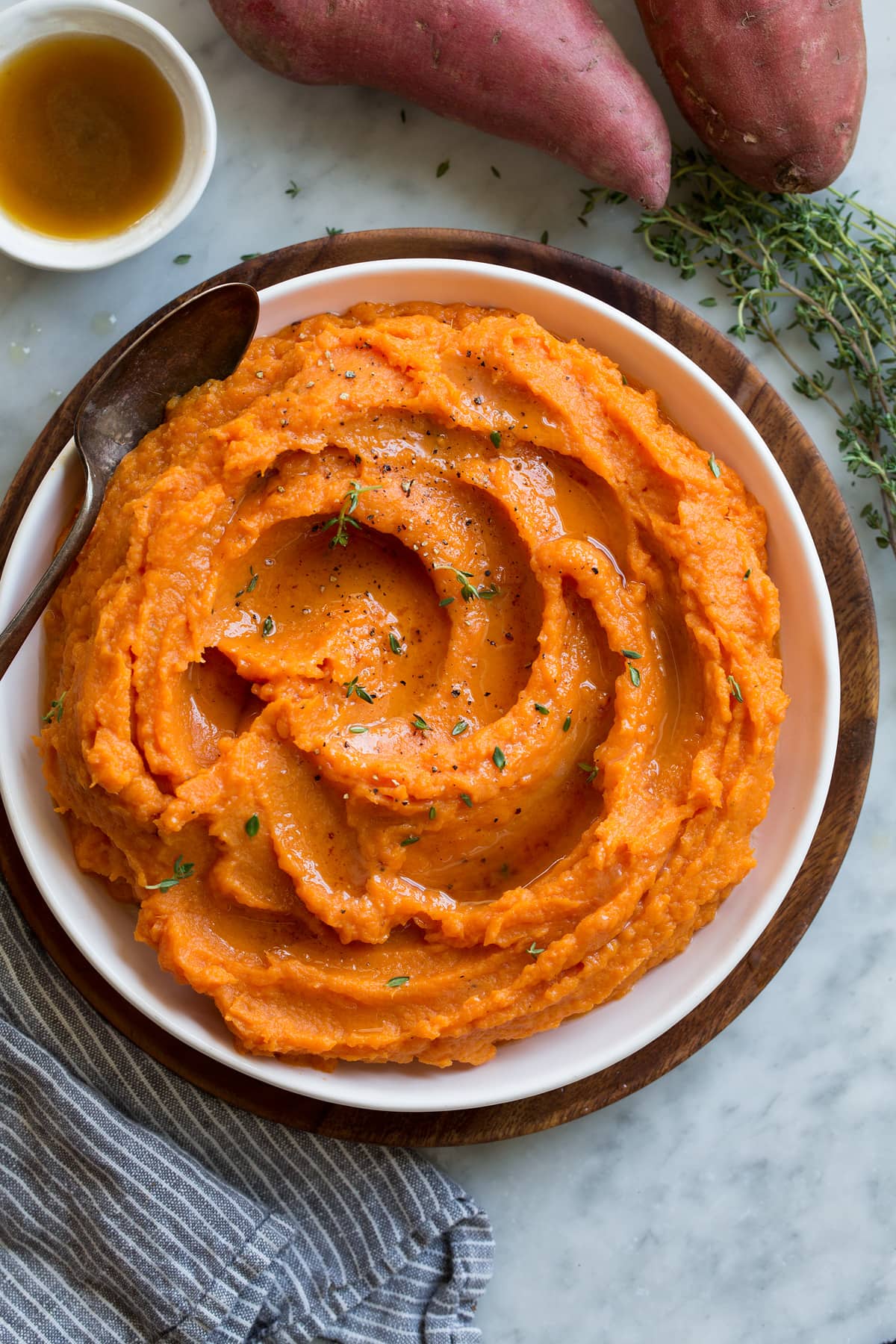 THE BEST MASHED SWEET POTATOES Overhead image of mashed sweet potatoes in a white serving bowl set over a wooden plate.