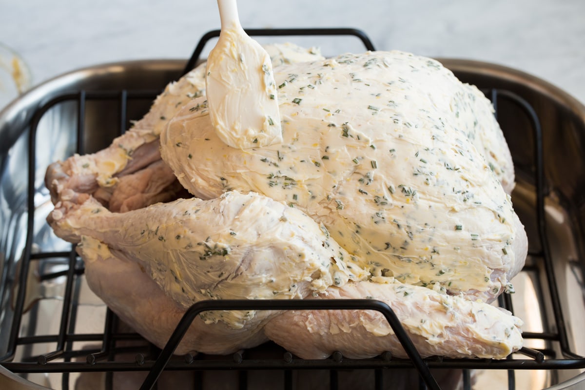 Roast Turkey - easy to follow recipe that turns out tender, juicy and full of flavor! A holiday staple! #turkey #thanksigiving Showing how to prepare a turkey for roasting. Brushing herb butter on large turkey in a roasting pan using a spatula.