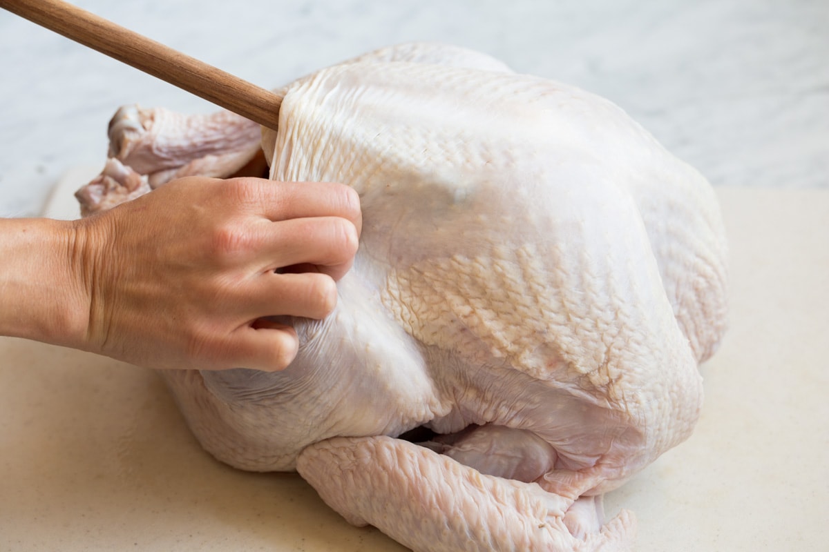 Roast Turkey - easy to follow recipe that turns out tender, juicy and full of flavor! A holiday staple! #turkey #thanksigiving Pressing back end of a wooden spoon into underside of turkey to create space to add butter.