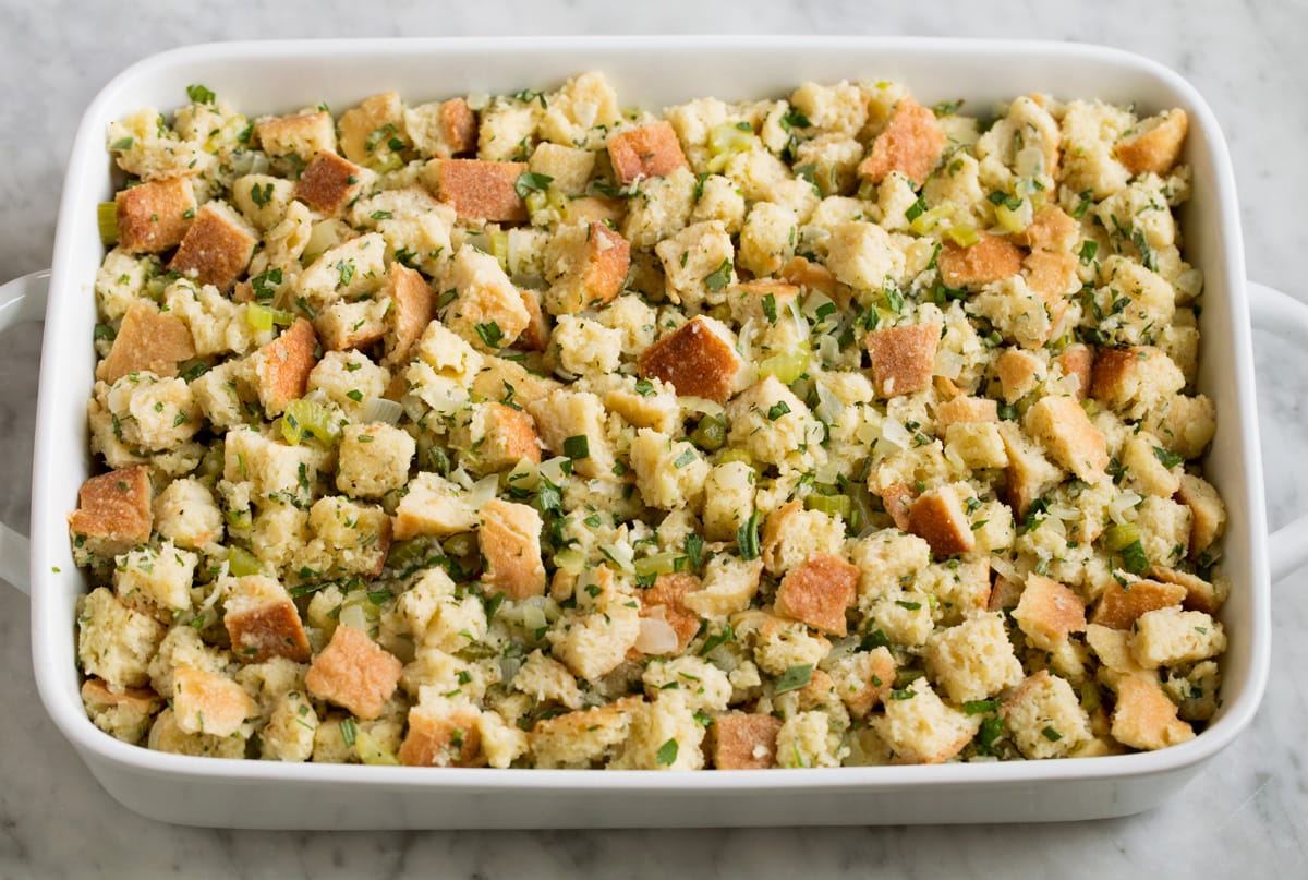 Stuffing Recipe - this is my FAVORITE stuffing! It's perfectly moistened in the center, browned and crisp on the edges and packed with butter and herb flavor. A fall staple! #stuffing #thanksgiving #sidedish #recipe Raw stuffing mixture spread in white baking dish shown before baking.