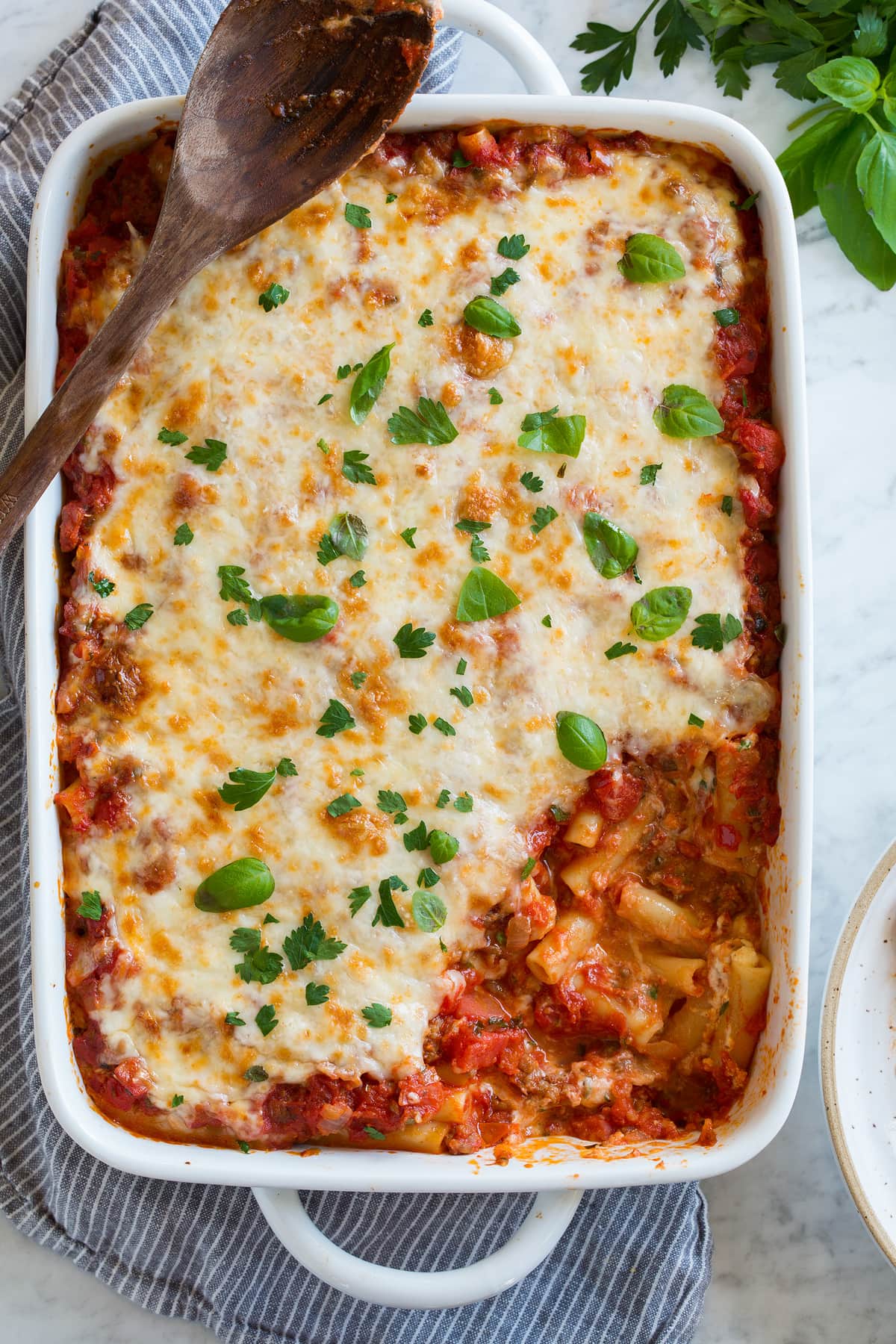 Baked Ziti Baked Ziti in a casserole dish shown after baking with a lightly golden browned cheese topping. One scoop is removed to show interior.