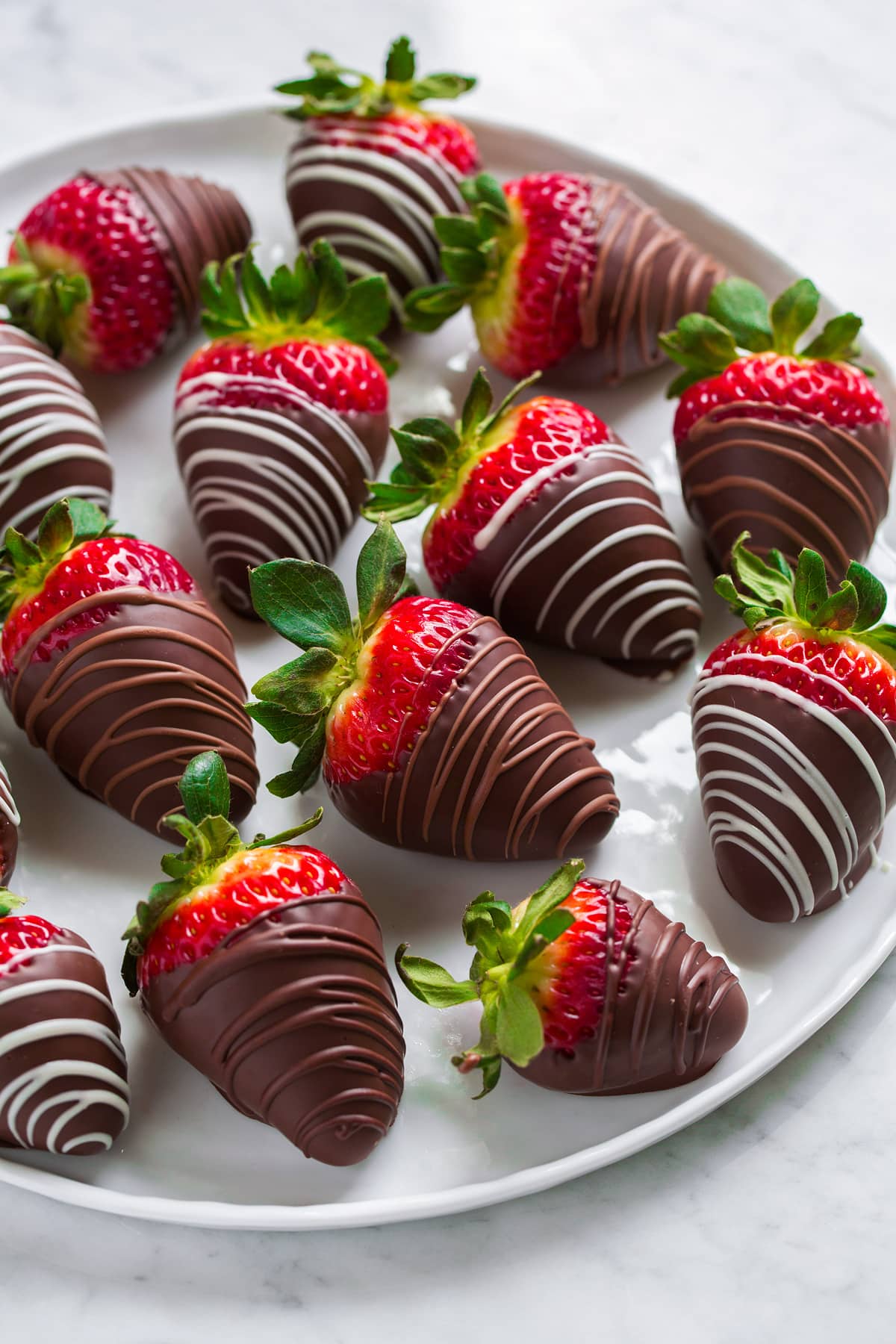 Chocolate Covered Strawberries Side view of chocolate covered strawberries sitting on a white serving platter on a marble surface.