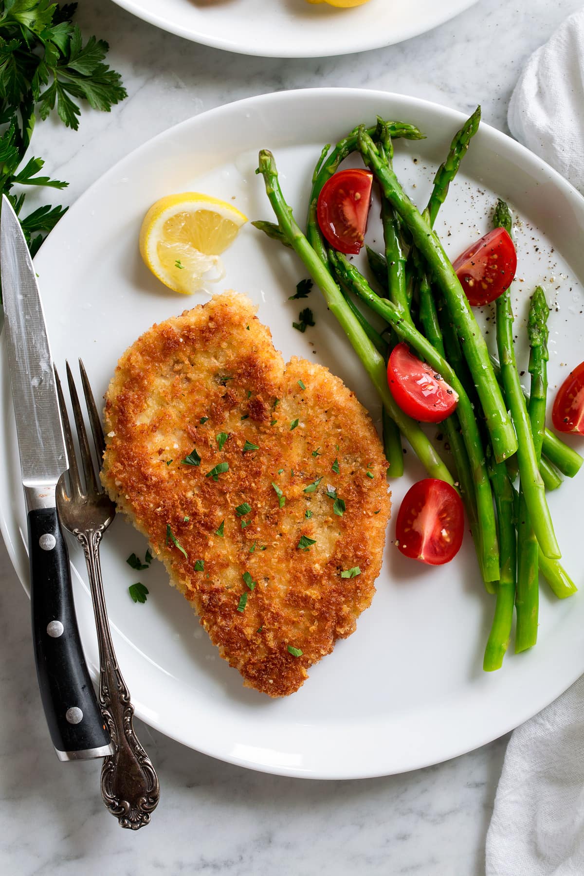 Parmesan Crusted Chicken Parmesan Crusted Chicken fried breast shown on a serving plate with a side of asparagus and tomatoes.