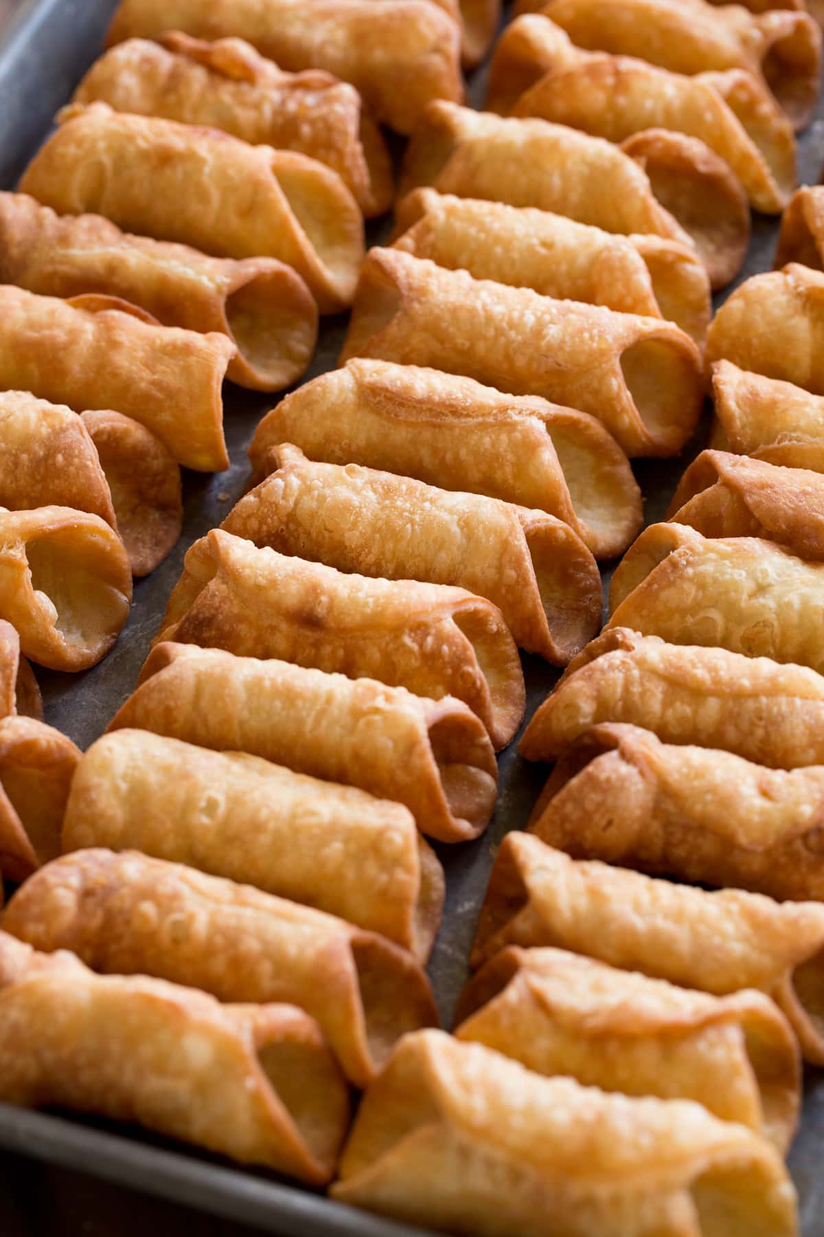 Cannoli Shells Homemade fried cannoli shells on a baking sheet shown before filling.
