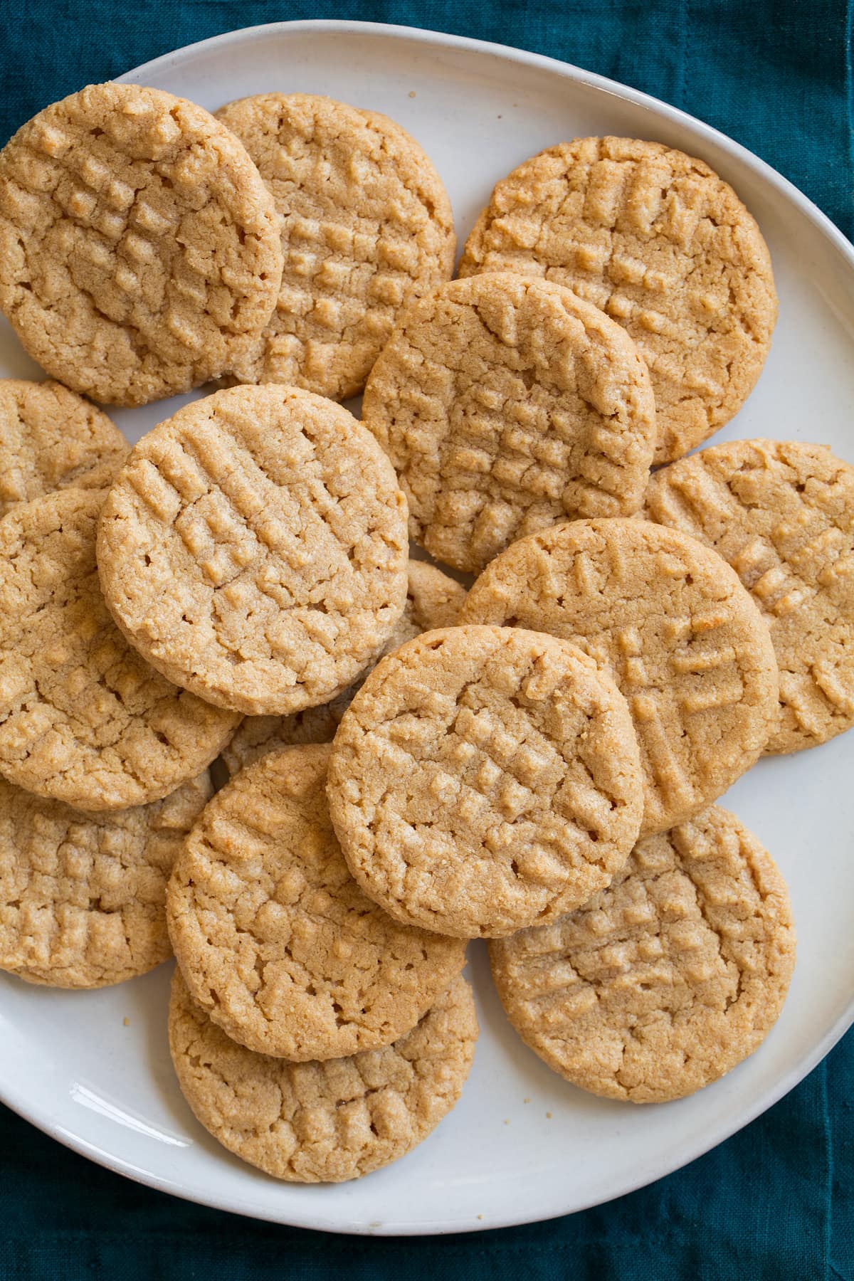 3-Ingredient Chocolate Chip Cookie 3 Ingredient Peanut Butter Cookies laying stacked on top of each other on a white serving plate.