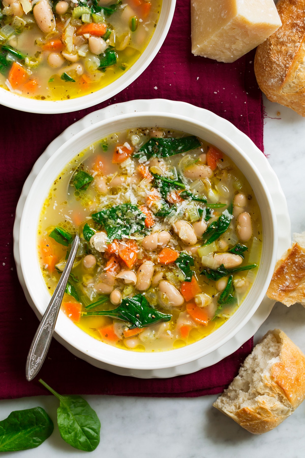 Bean Soup {Tuscan Style} White bowl with tuscan bean soup set over a white scalloped plate and a red napkin.