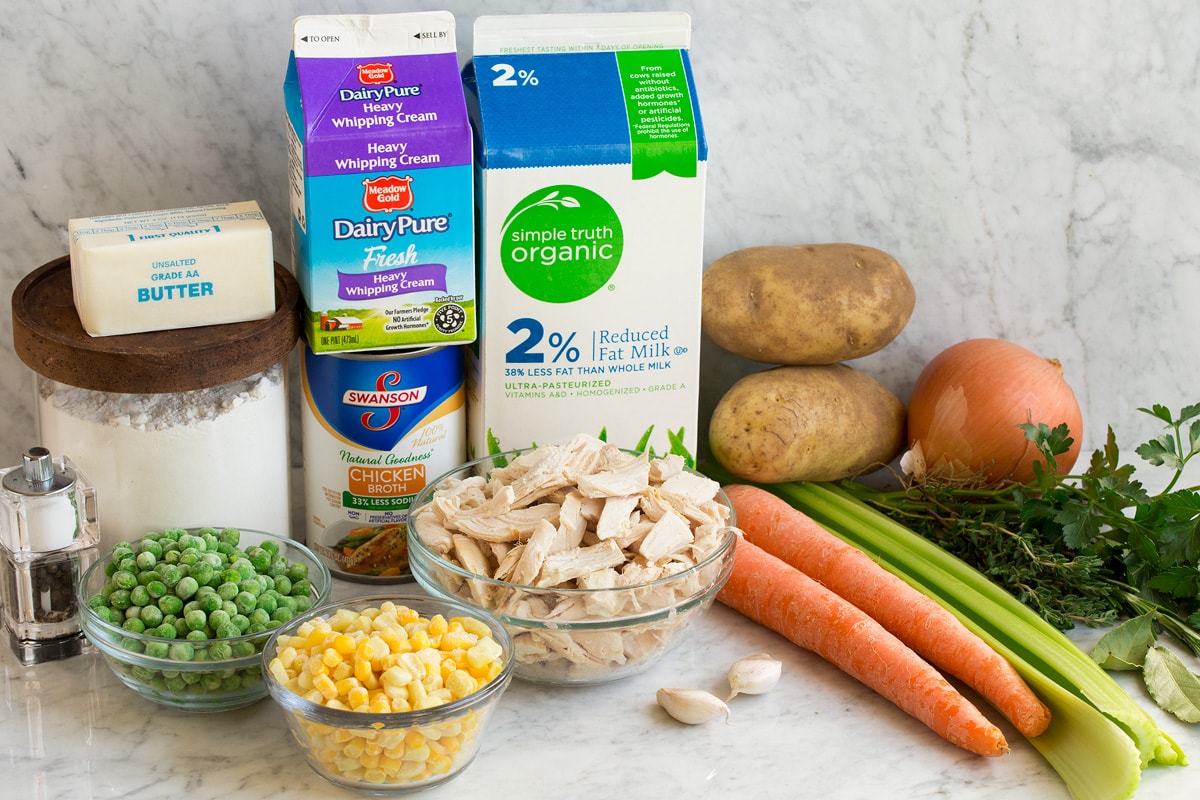 Chicken Pot Pie Soup Image showing ingredients needed to make chicken pot pie soup including milk, cream, chicken broth, flour, butter, peas, corn, chicken, carrots, celery, potatoes, onion, garlic and fresh herbs.