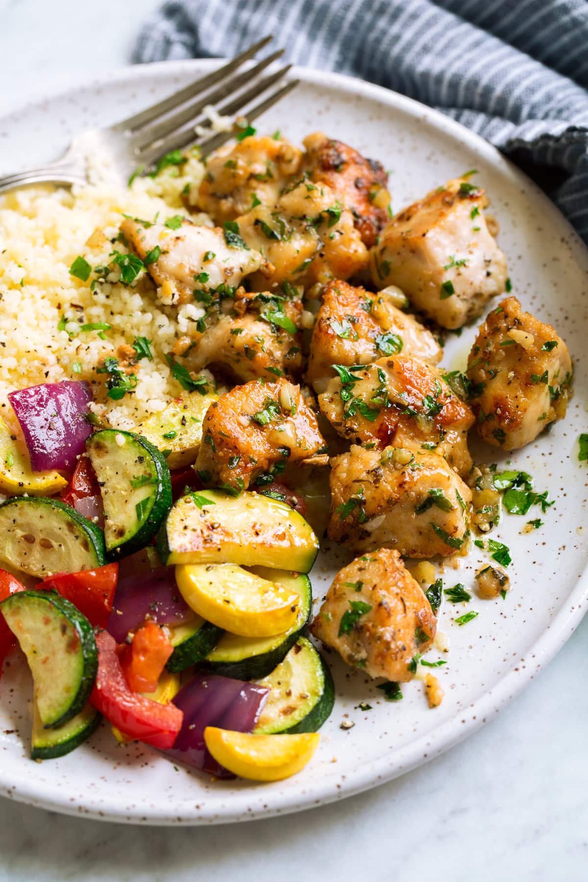 Garlic Butter Chicken Bites Chicken bites on a white serving plate with a side of couscous and vegetables.